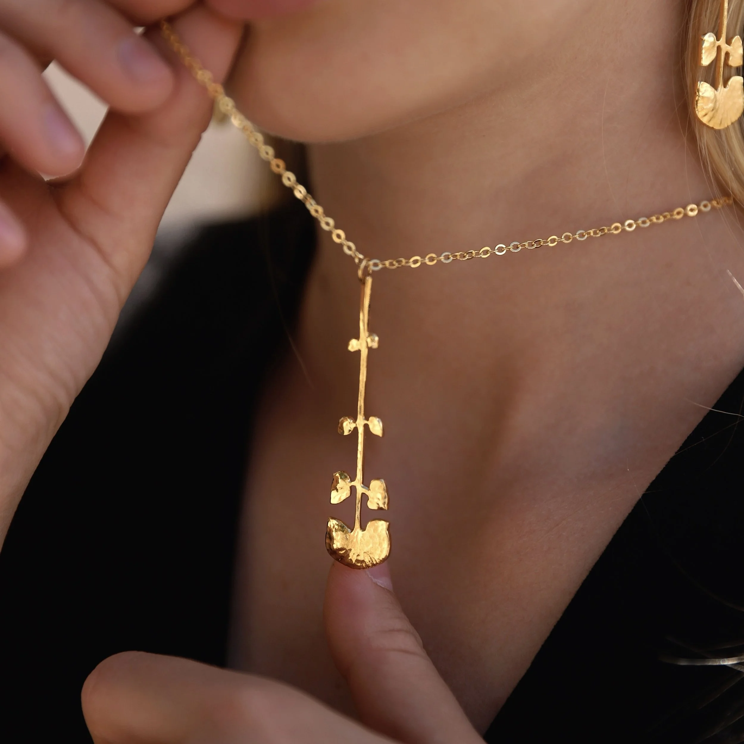 Gold necklace with a pendant shaped like a branch or a stylized tree.
