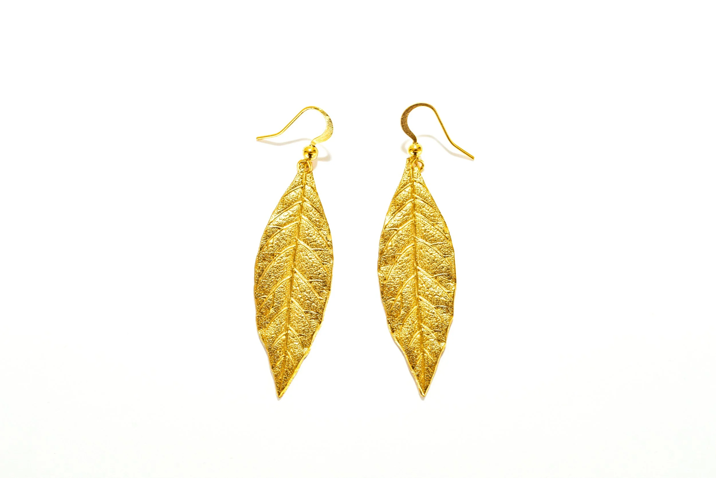 Gros plan sur les boucles d'oreilles feuilles de laurier, détail du motif et de la finition dorée