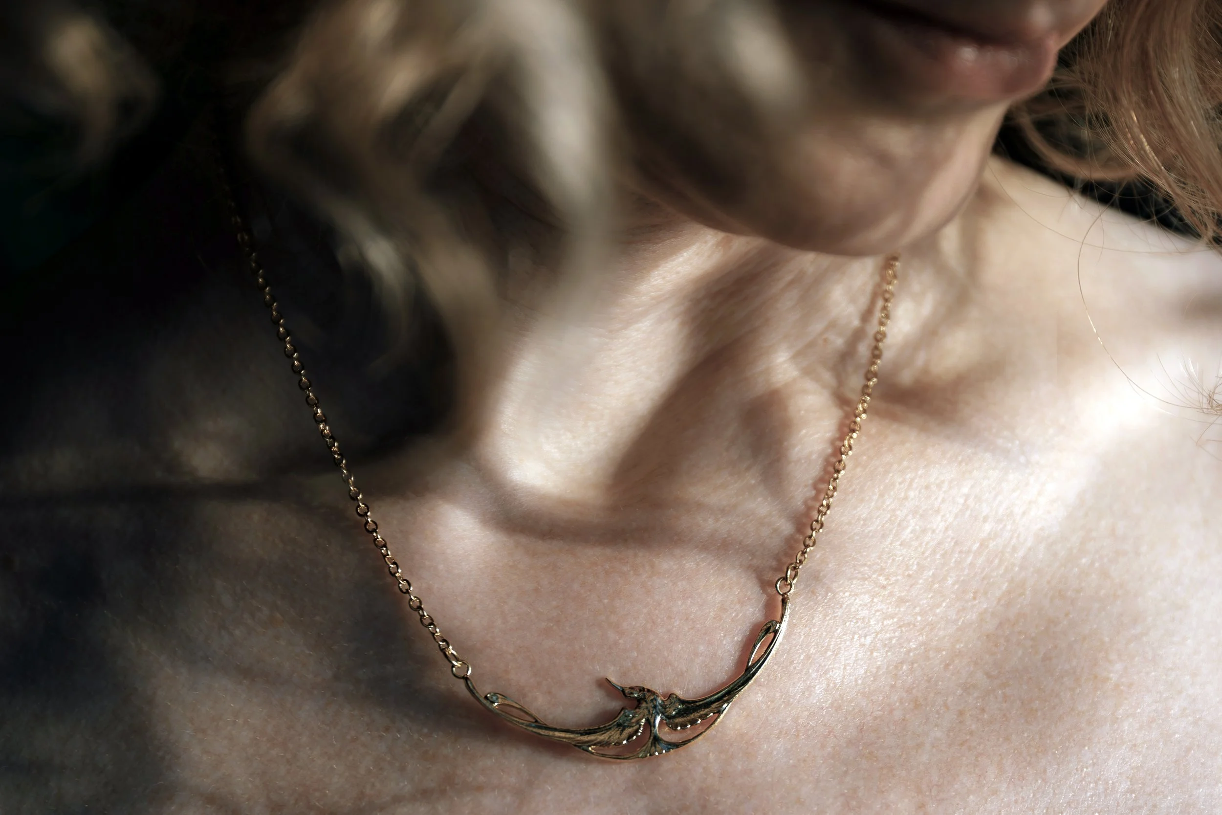 Gros plan sur le collier cigogne, détail du motif et de la finition dorée