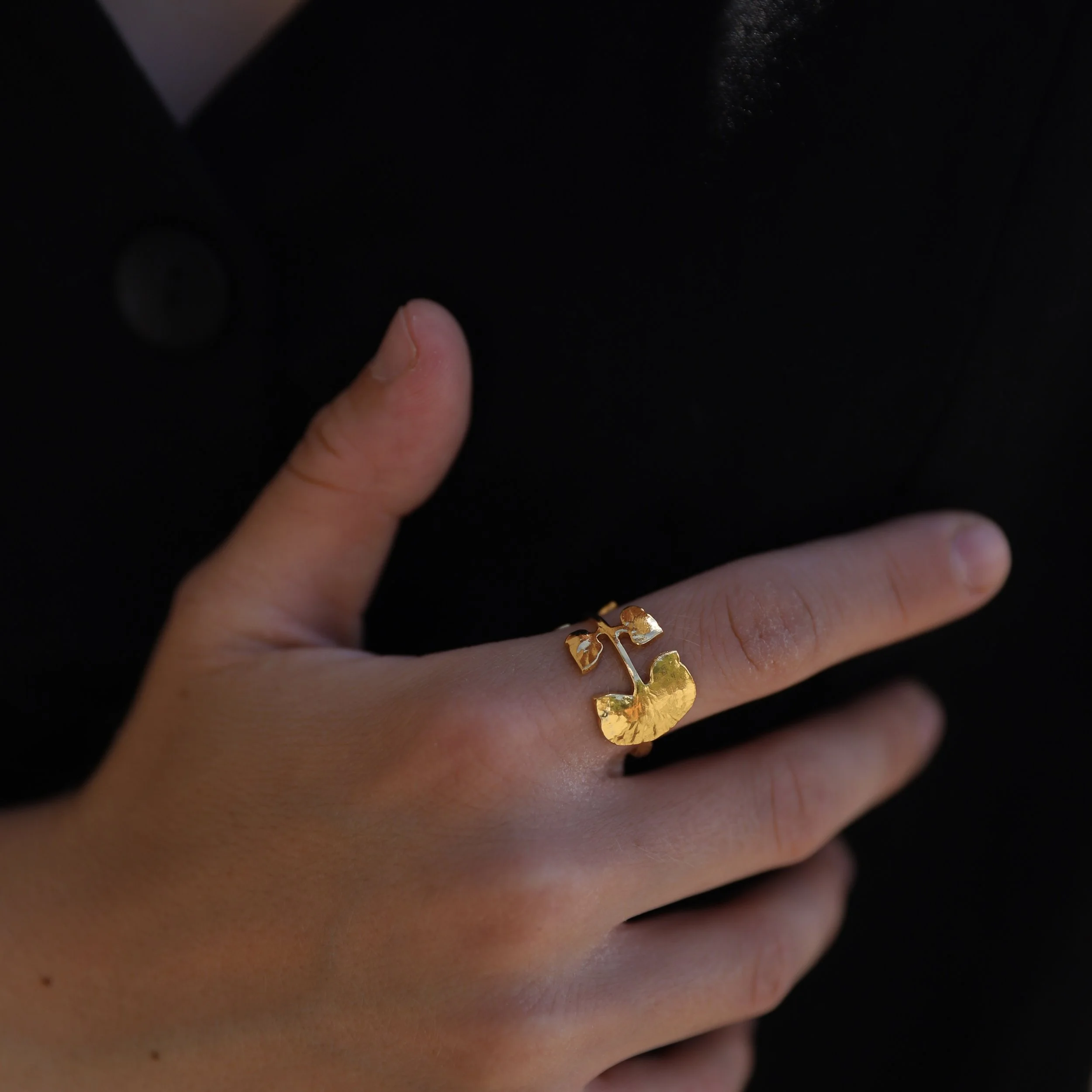 A hand wears a gold apple-shaped ring on the ring finger.