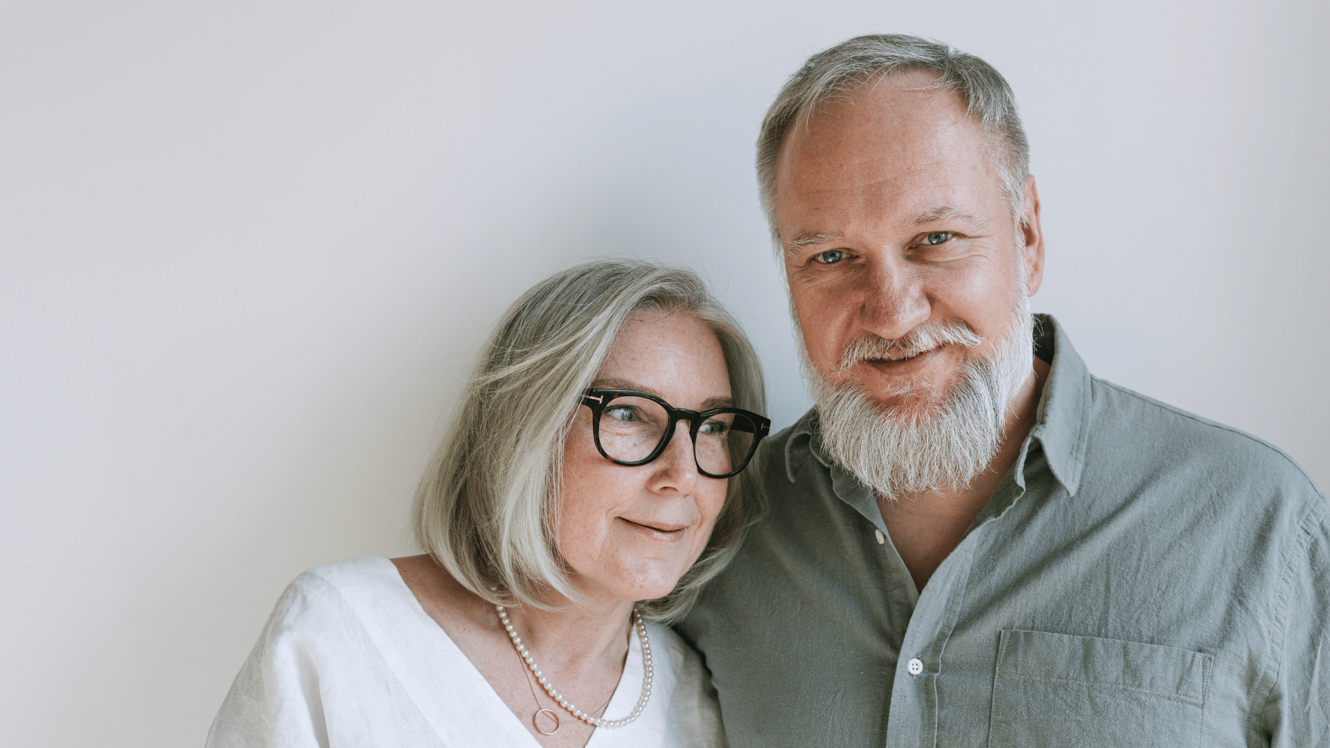 Older man smiling at camera and stood with his wife