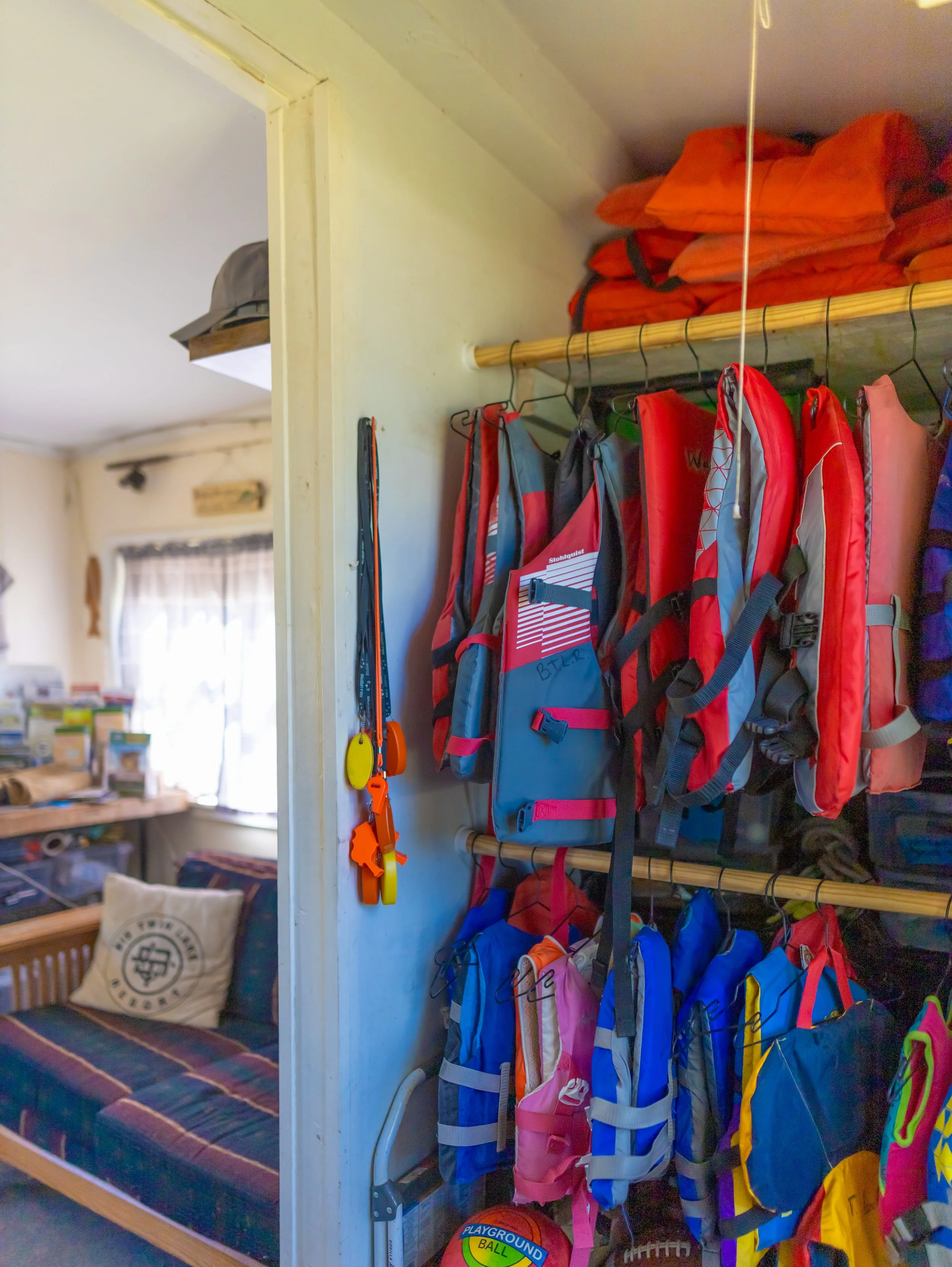 A closet with colorful backpacks and orange sleeping bags on shelves, with outdoor gear hanging nearby.