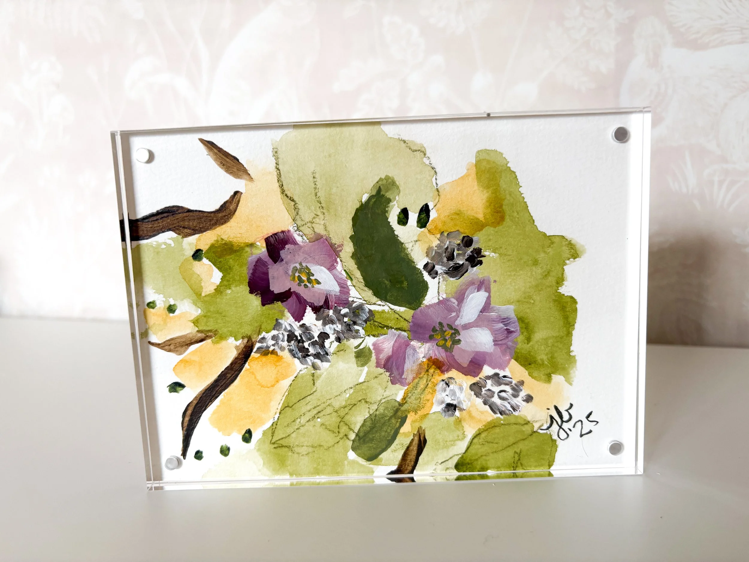 Watercolor painting of lilac flowers and green leaves in a glass frame, signed and dated 'A.L. '25'.