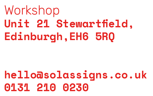 Sign with workshop address, contact info, and website in red text on a white background.
