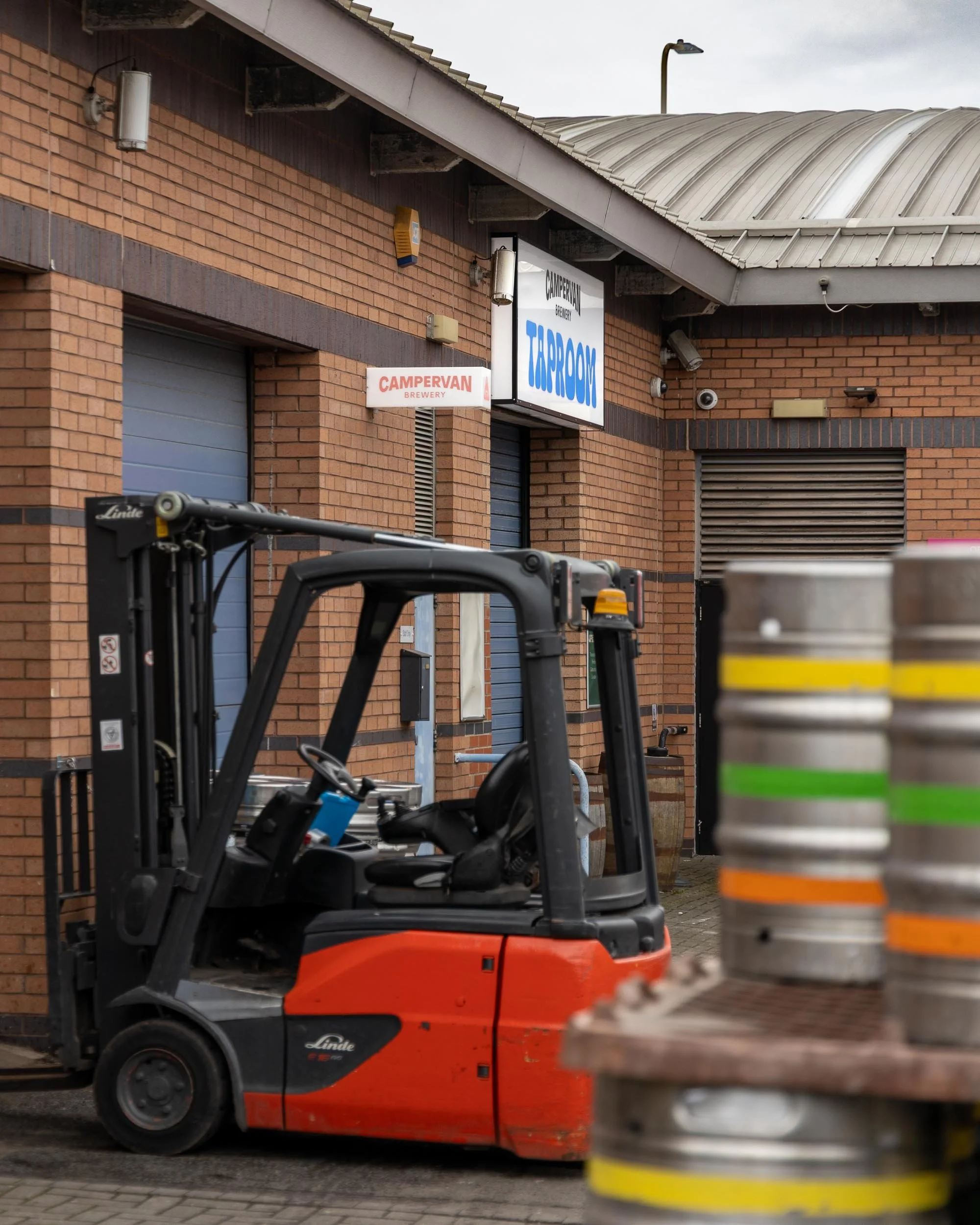 A forklift parked outside a brick building with signs for Campervan Brewery and Taroom. There are beer kegs stacked in the foreground.