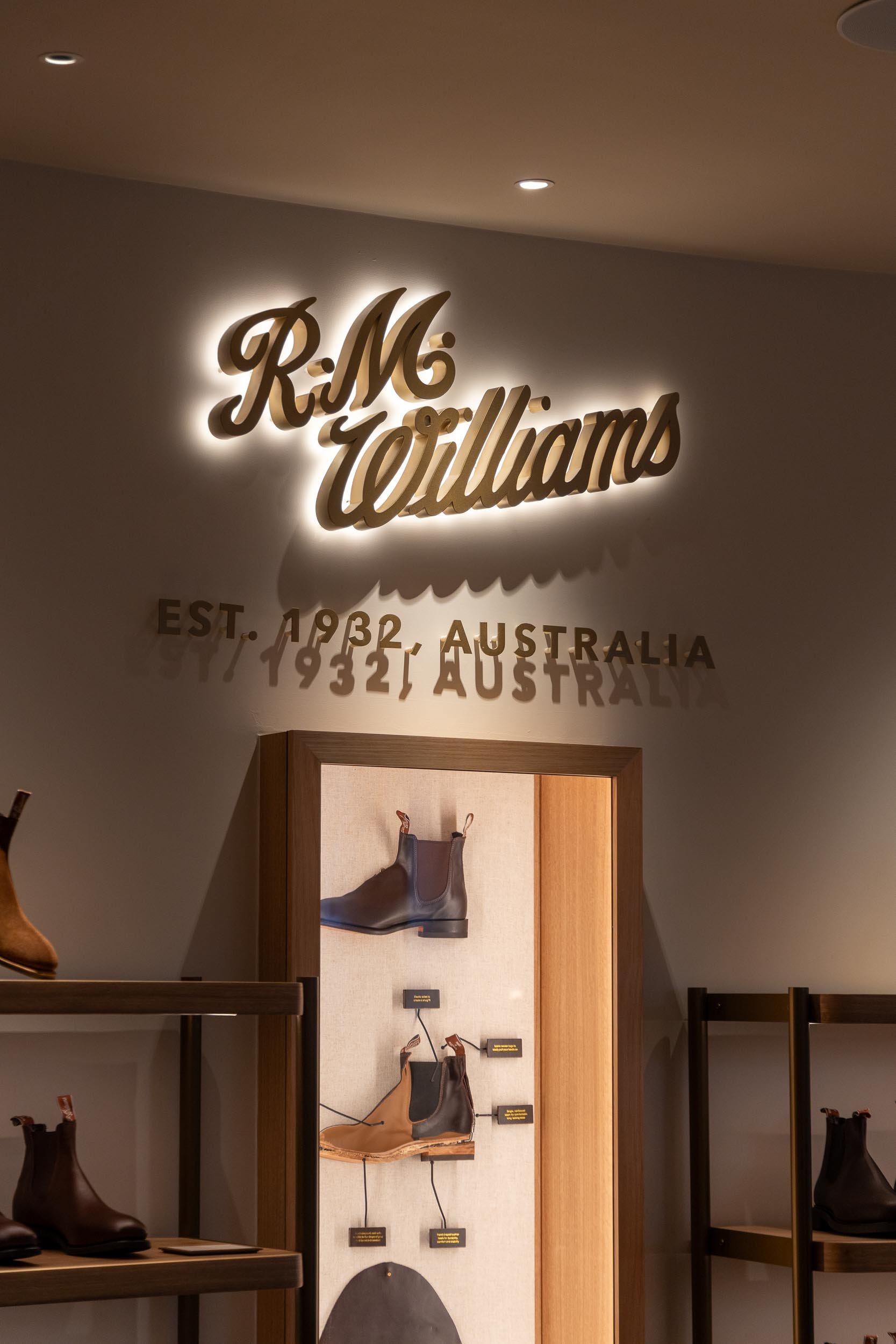 Sign reading 'R.M. Williams' with establishment year 1932 in Australia, illuminated on the wall above a display of boots.