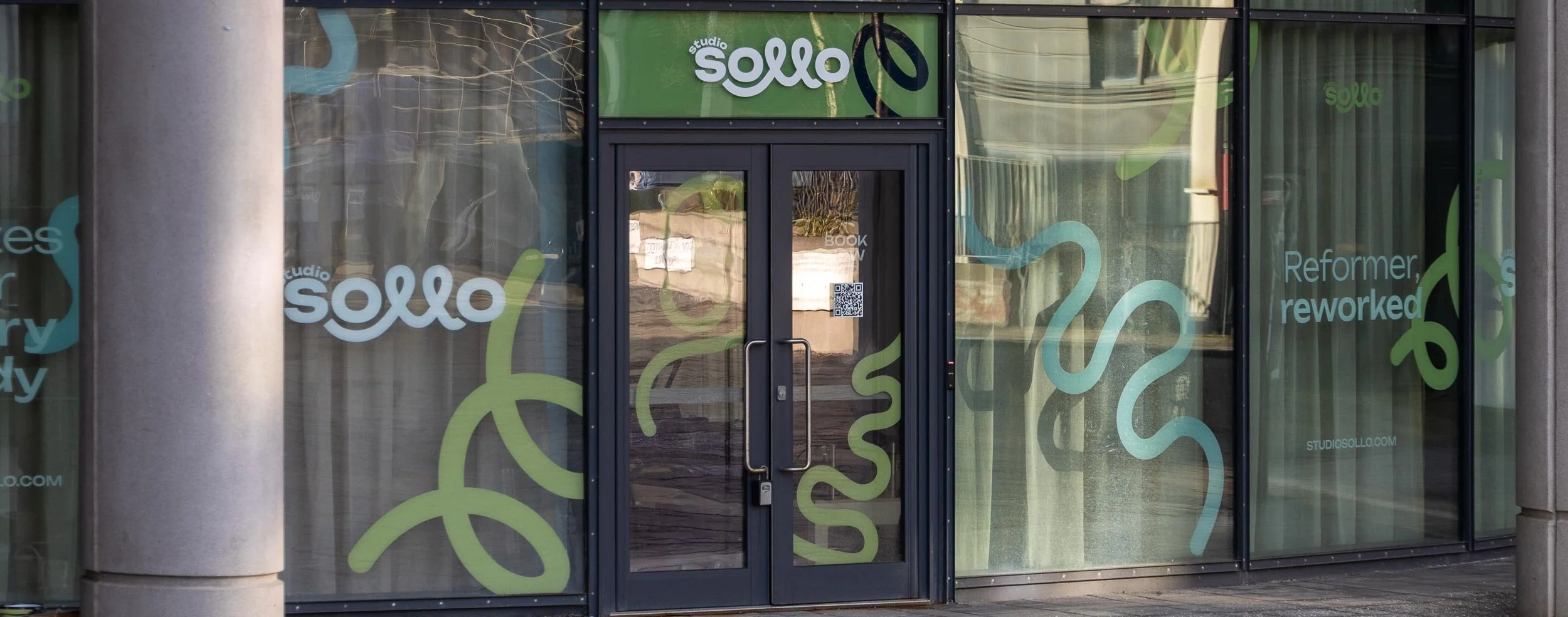Storefront of Studio Sollo with glass windows decorated with abstract green and blue lines and the text "Reformer reworked" and "studio sollo" displayed.