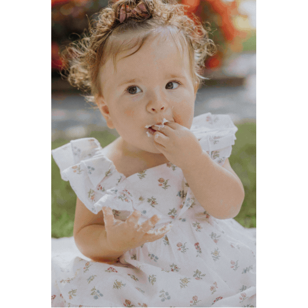 A young girl with curly hair and a bowler hat eating ice cream outdoors during daytime.