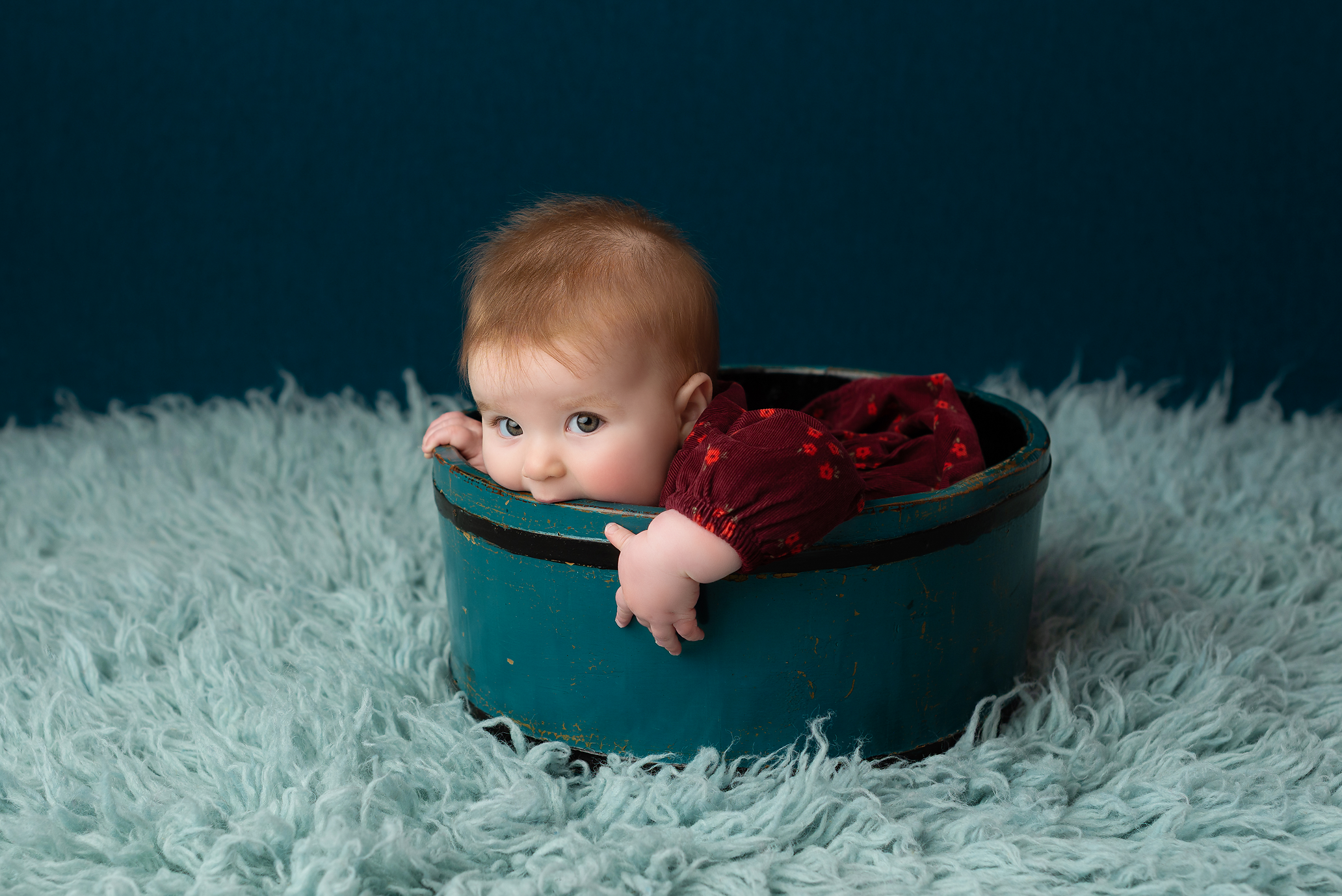 baby girl in burgundy dress biting teal bucket