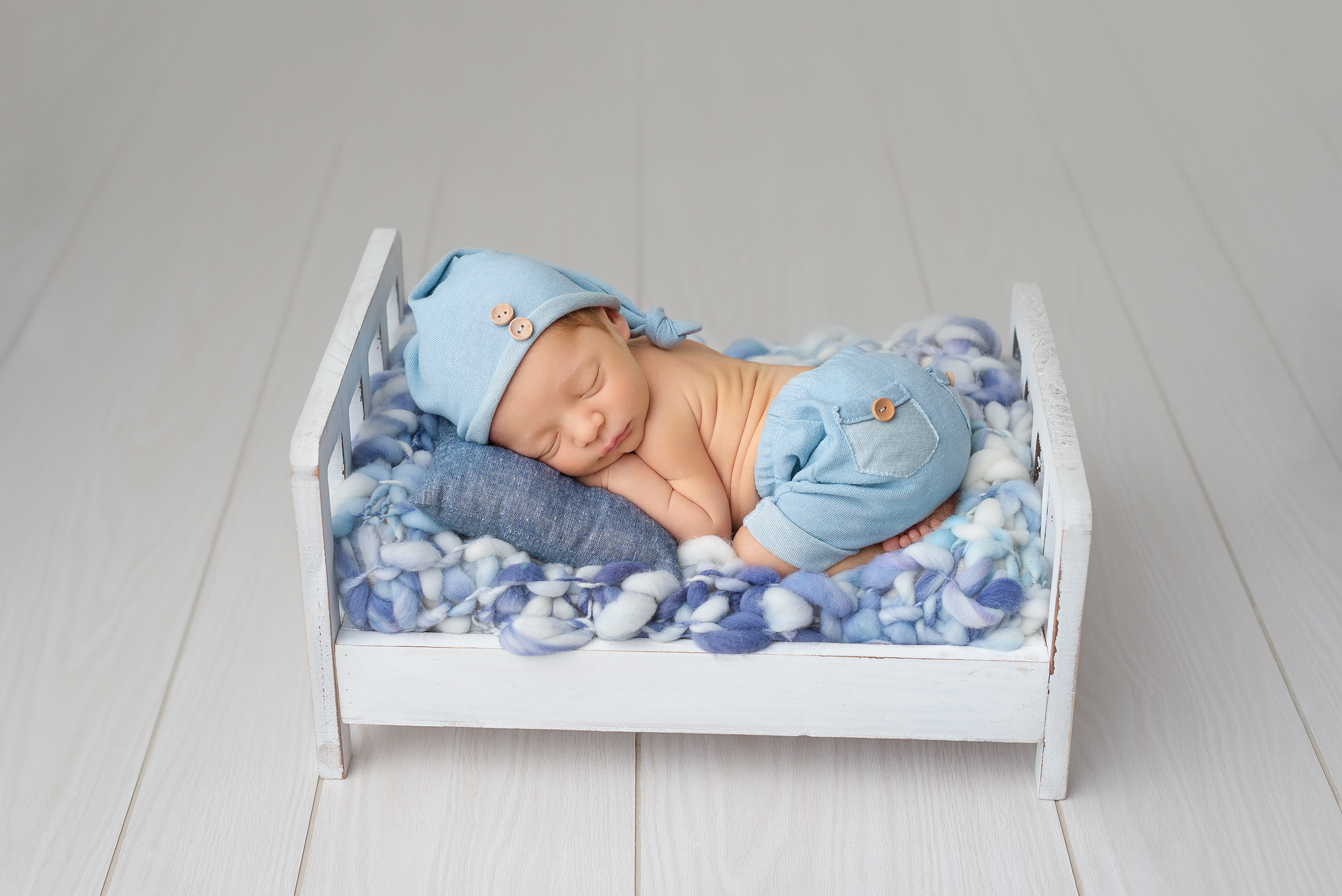 baby boy in blue shorts and hat with blue knit blanket on bed