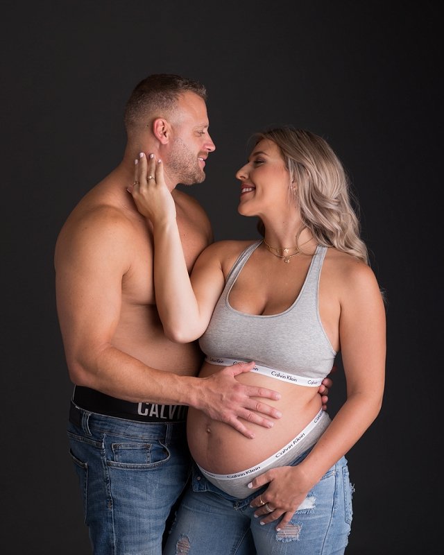 pregnant mother in jeans and Calvin Klein sports bra with husband in jeans