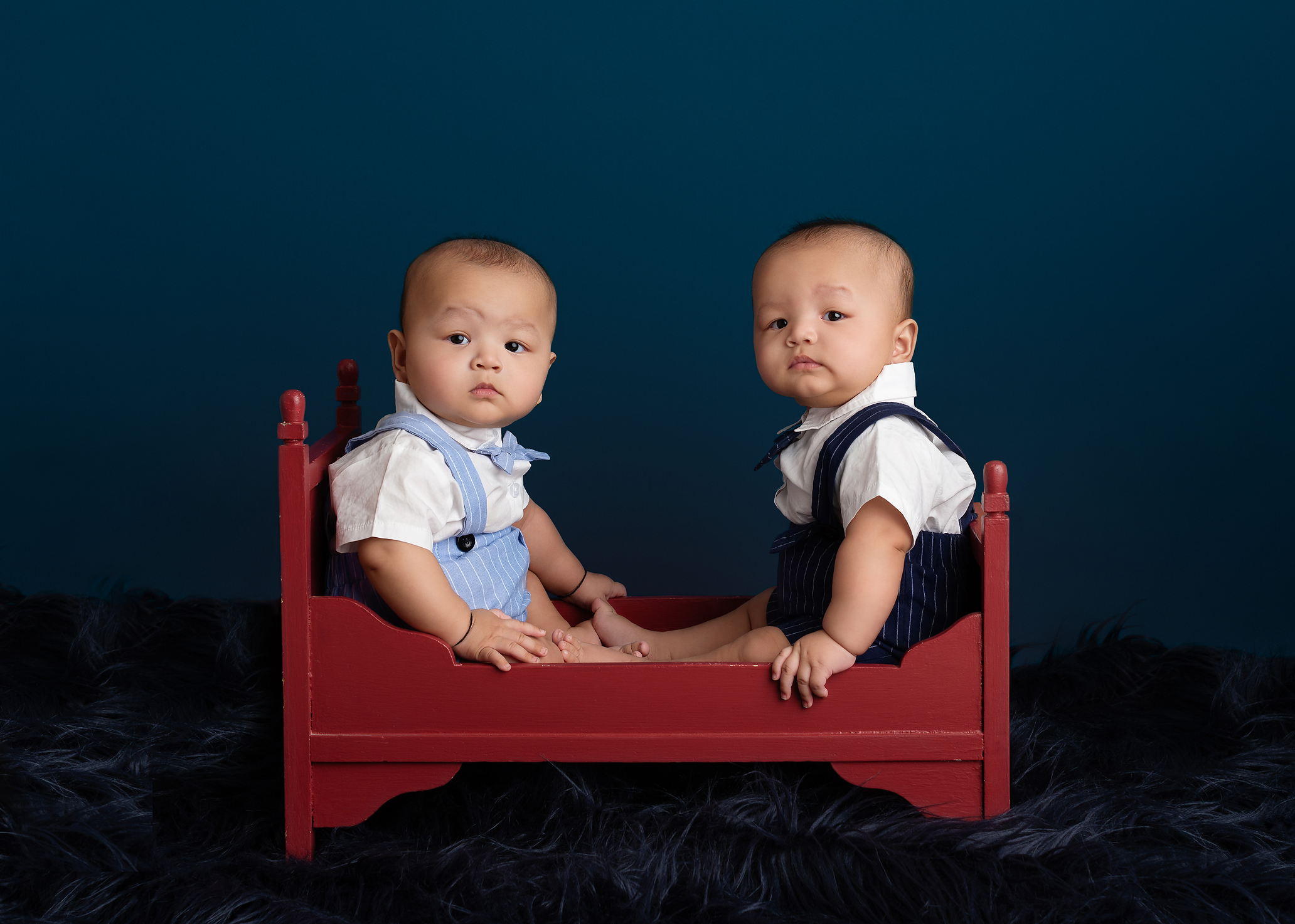 twin baby boys sitting in red bed