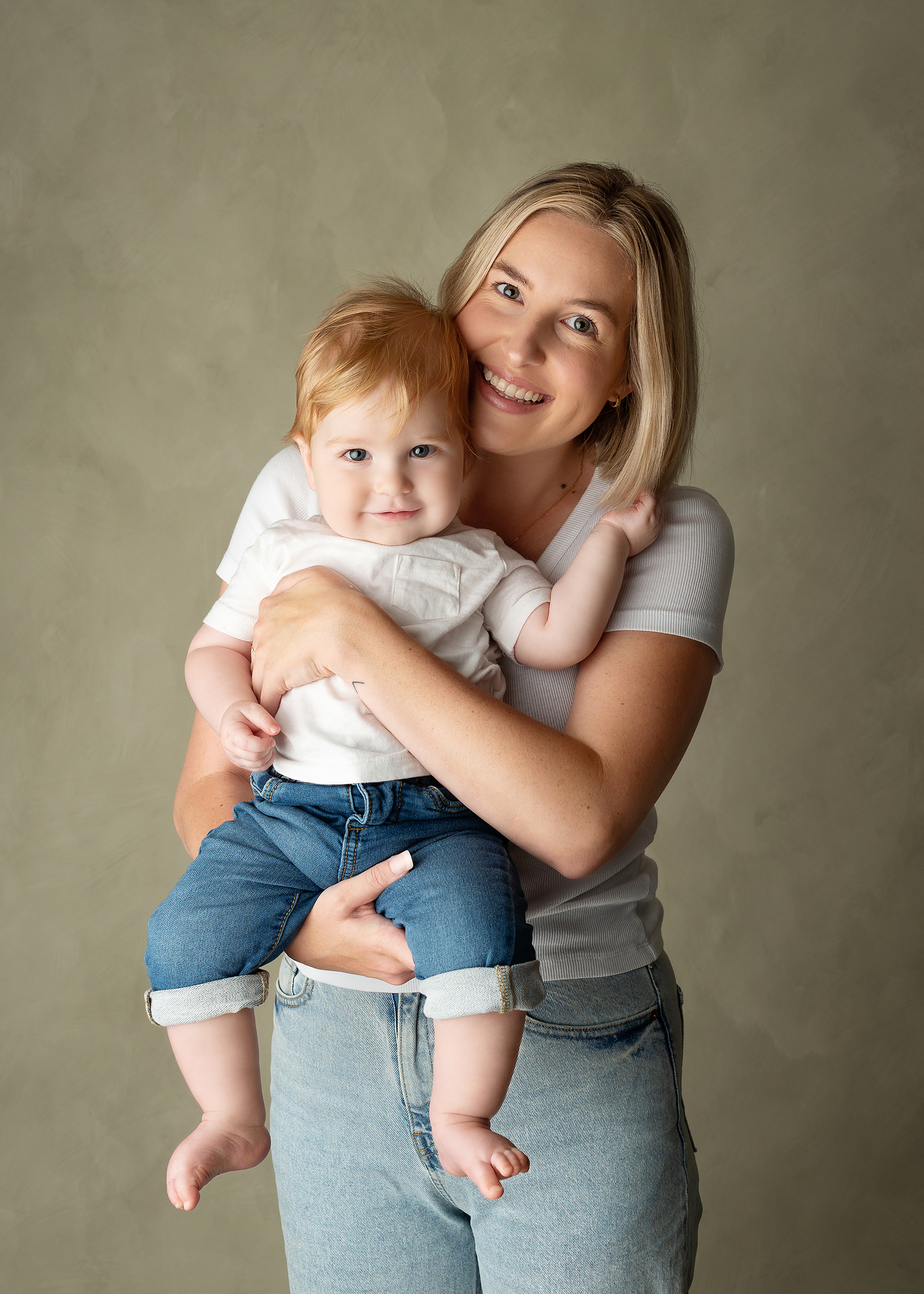 mom holding onto baby, both in jeans in portraits