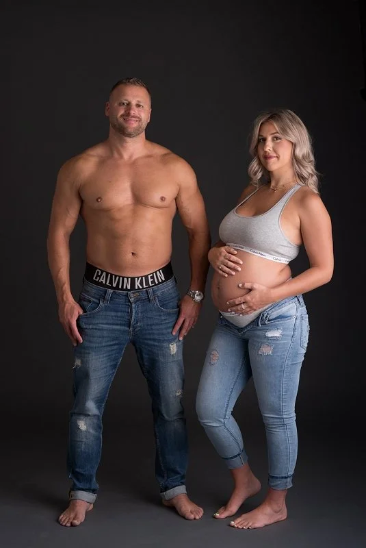 pregnant mother in jeans and Calvin Klein sports bra with husband in jeans