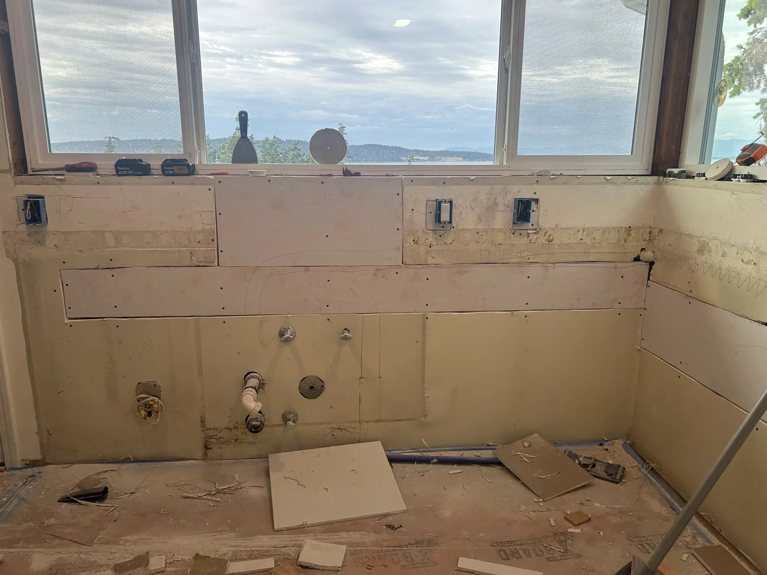 Kitchen under renovation, wall with electrical and plumbing fixtures, window with scenic view of mountains and water.