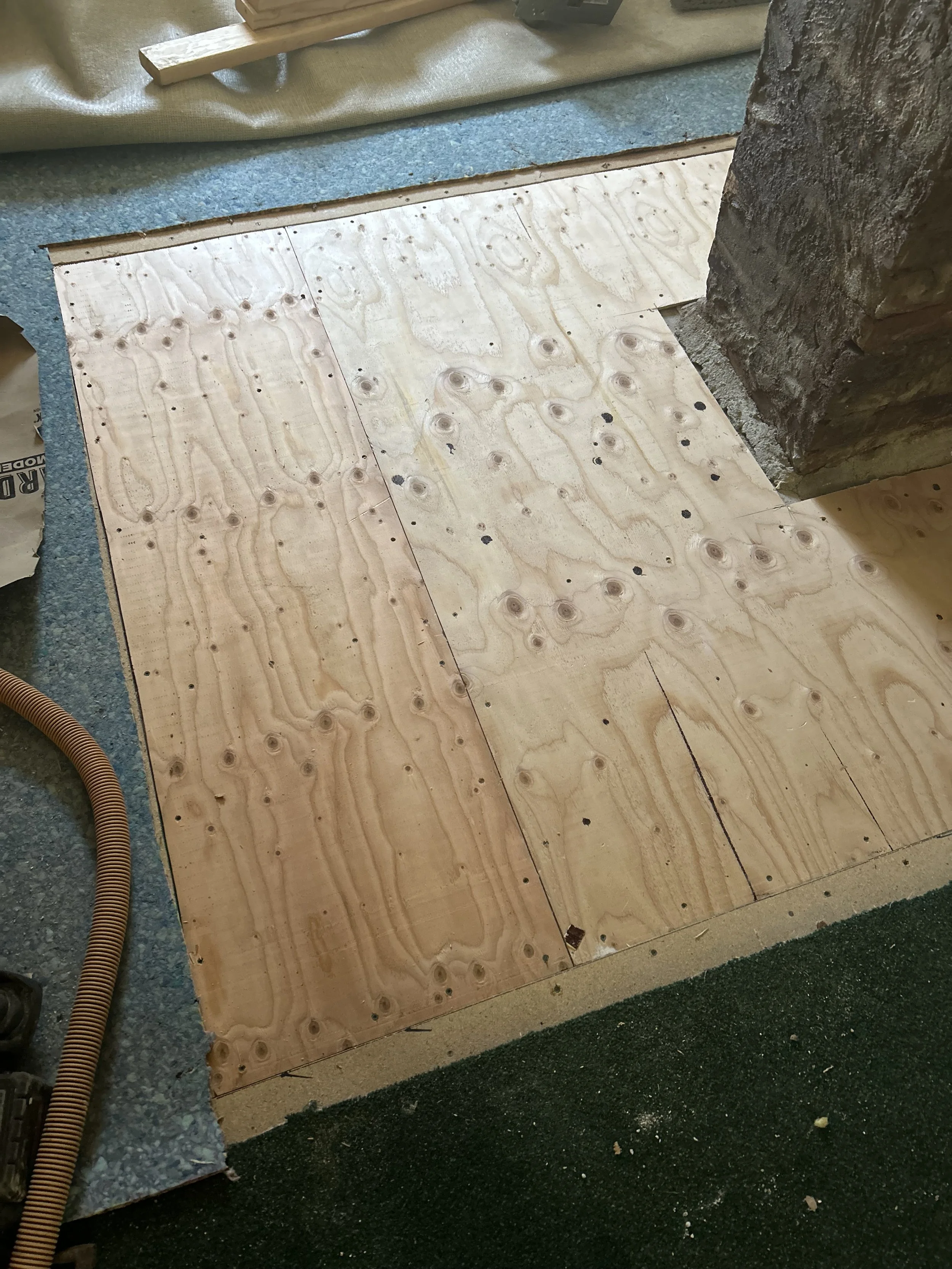 Plywood subflooring installed on a floor, with a brick fireplace on the right side.
