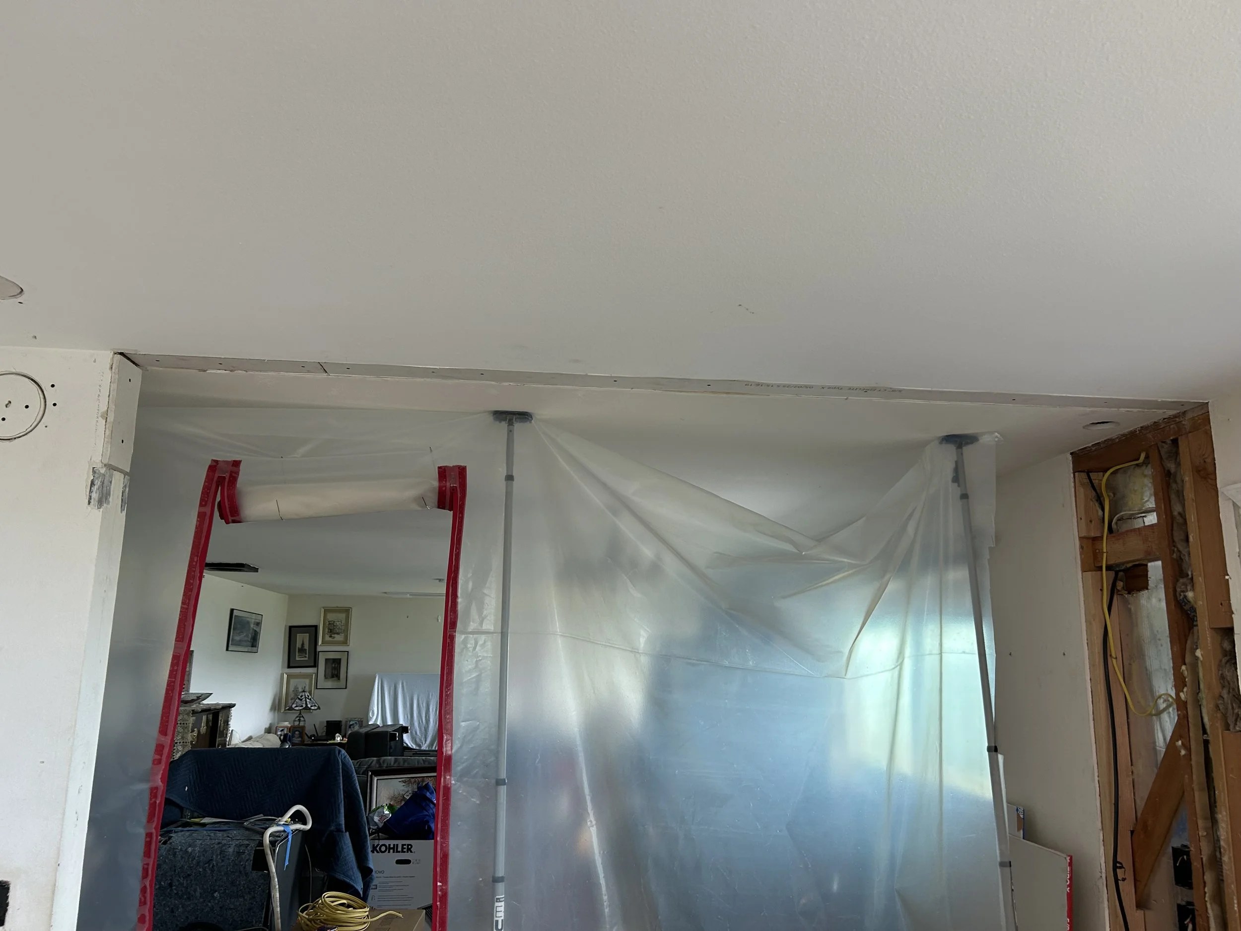 Interior of a room under renovation with plastic sheeting and metal support poles.