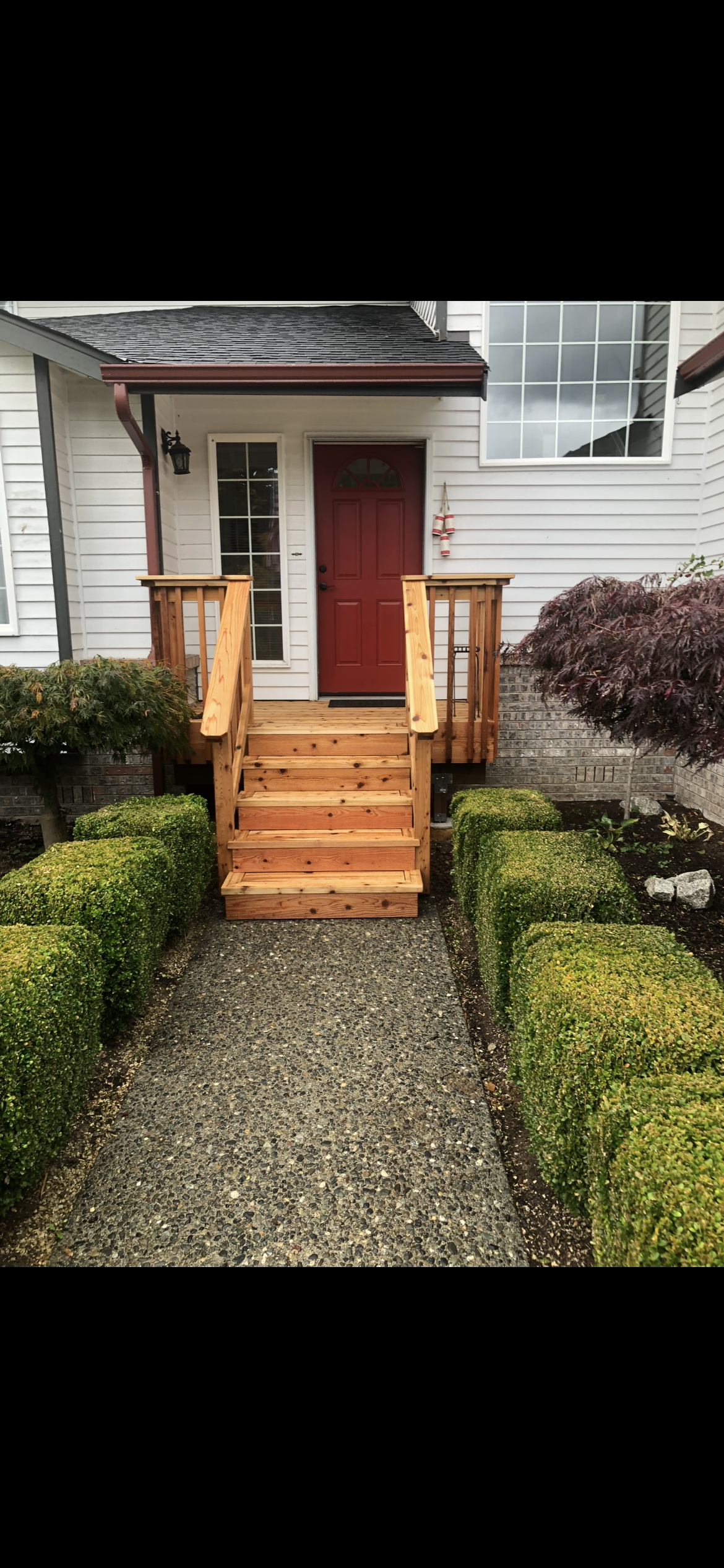 Front porch with red door, wooden stairs, and landscaped bushes.
