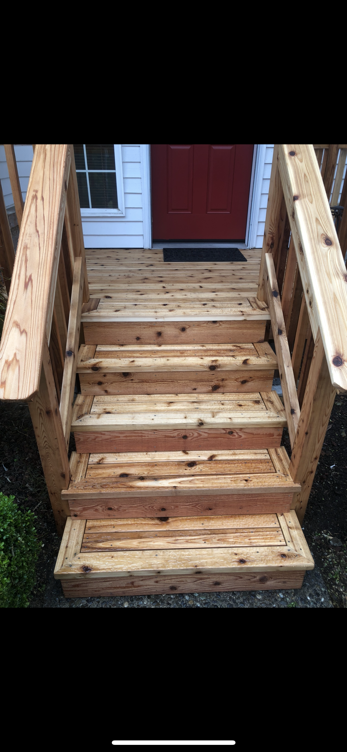 Wooden front porch with stairs leading up to a door painted red, white siding on the house, and a small window to the left of the door.