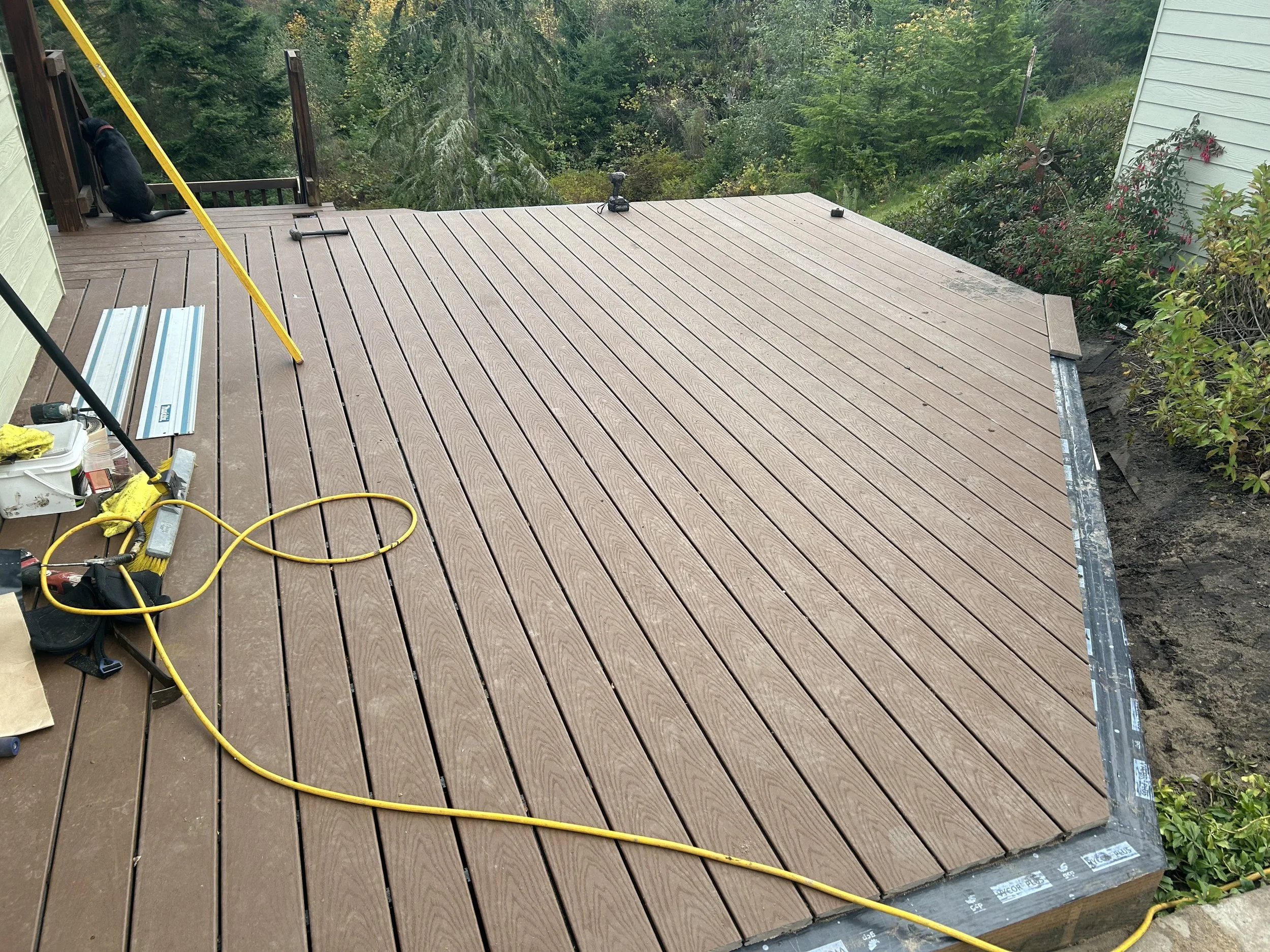 Newly installed wooden deck with construction tools and equipment, surrounded by greenery.