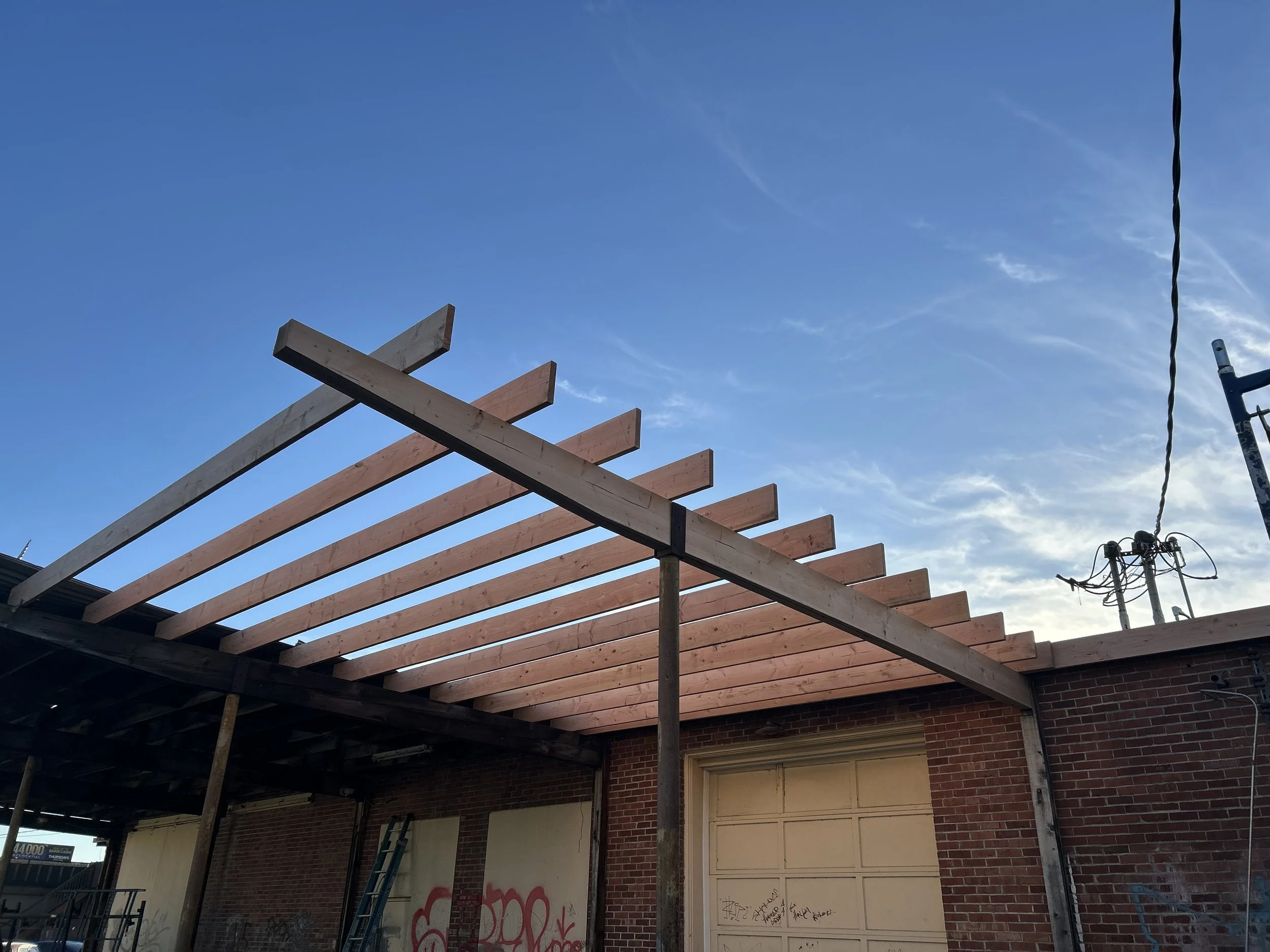Construction of a new wooden roof frame on a brick building under a clear blue sky.