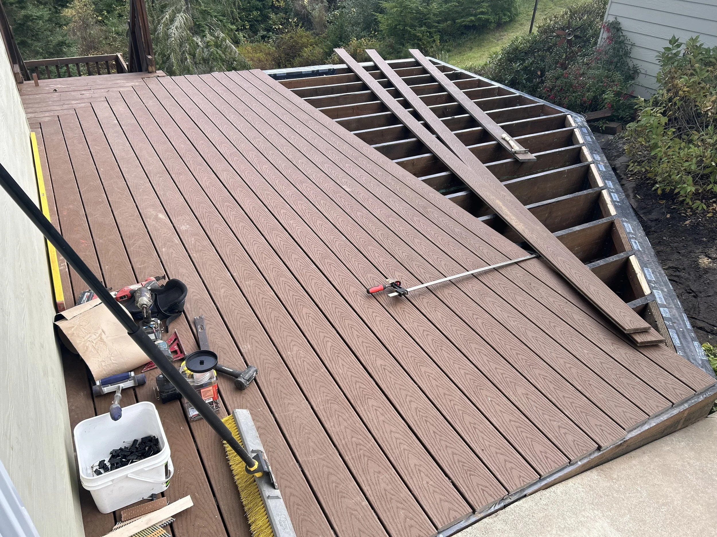 Installing a new wooden deck with brown planks on an outdoor patio, with tools and materials nearby, and an unfinished section showing the underlying frame.