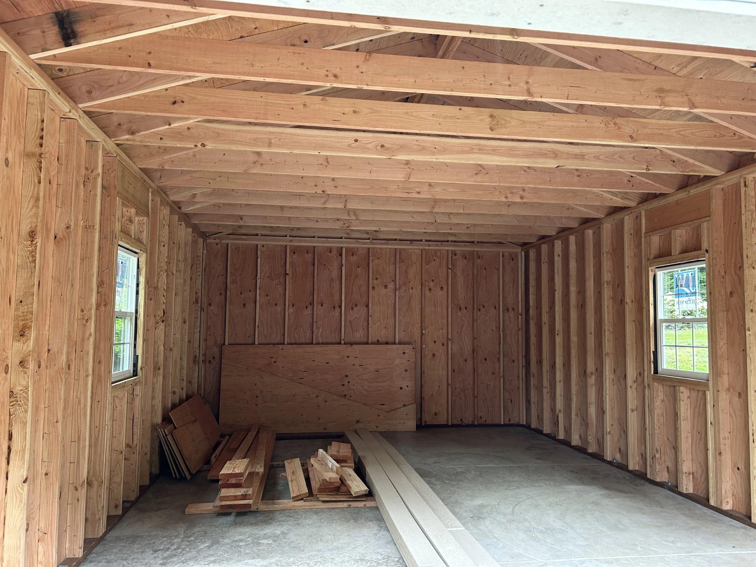 Interior of a room under construction with wooden framing, two small windows, and various wood pieces and lumber on the floor.