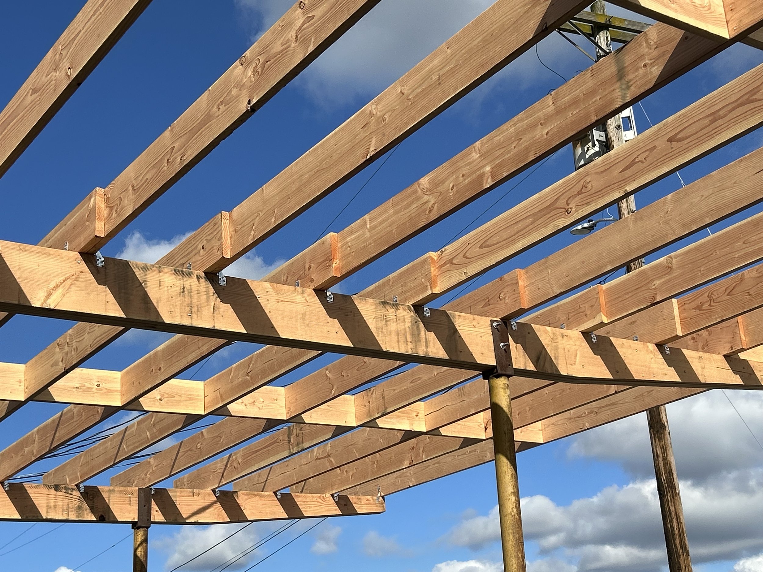 Wooden framework for a structure under construction against a blue sky with clouds and a utility pole in the background.