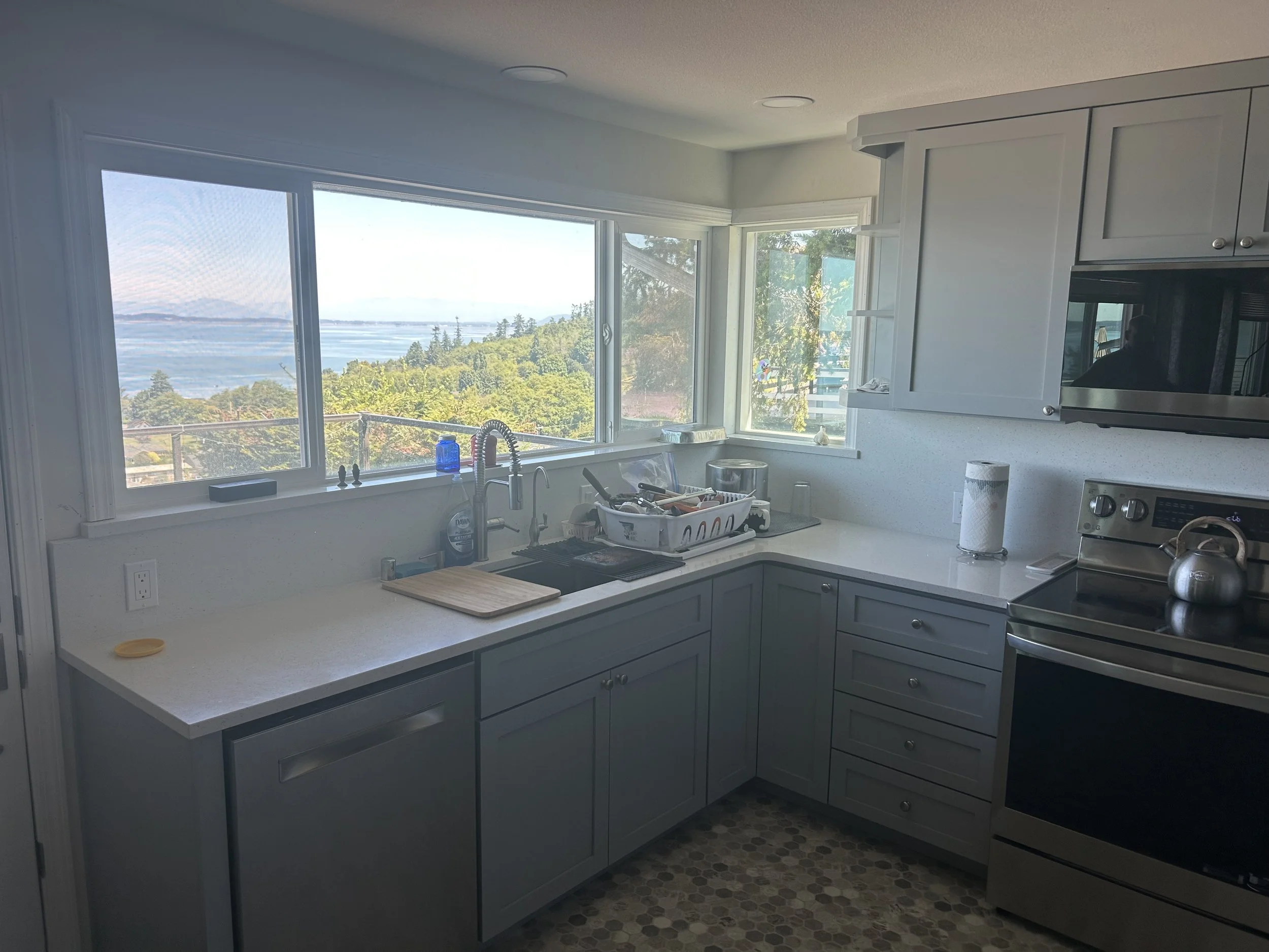 Kitchen with white cabinets and a large window overlooking a scenic view of trees, water, and sky.