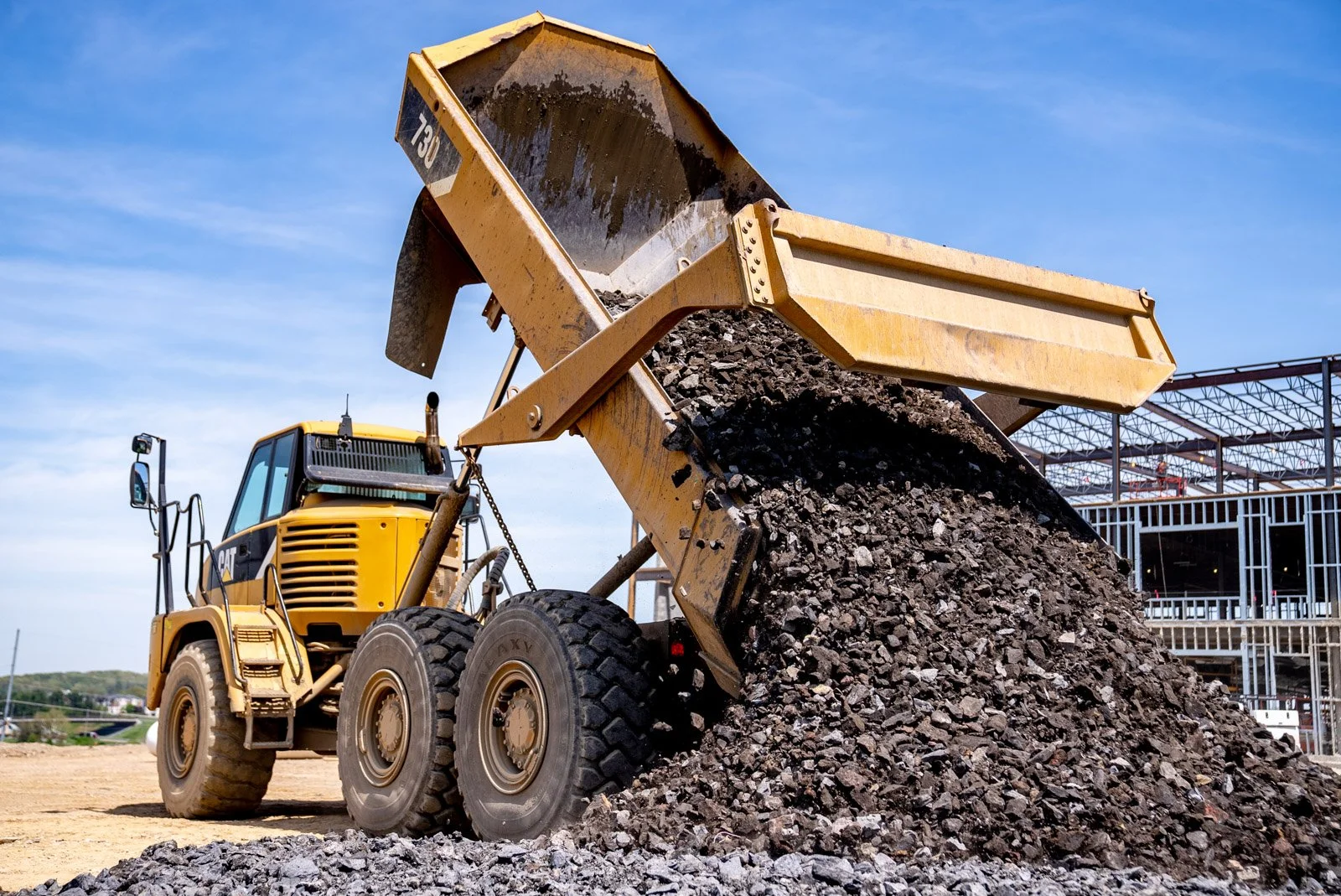 A yellow Caterpillar front loader dumping a load of dirt or gravel on a construction site under a blue sky.