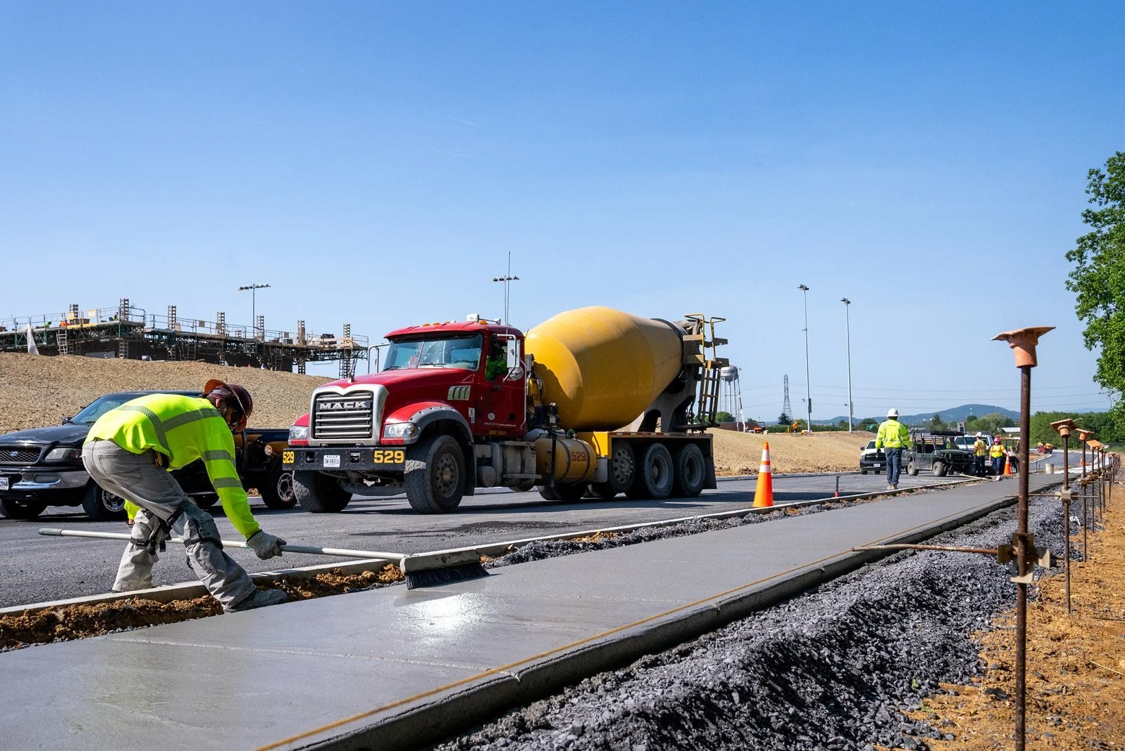 Construction workers pouring concrete on a road with a cement mixer truck in the background and construction equipment around.