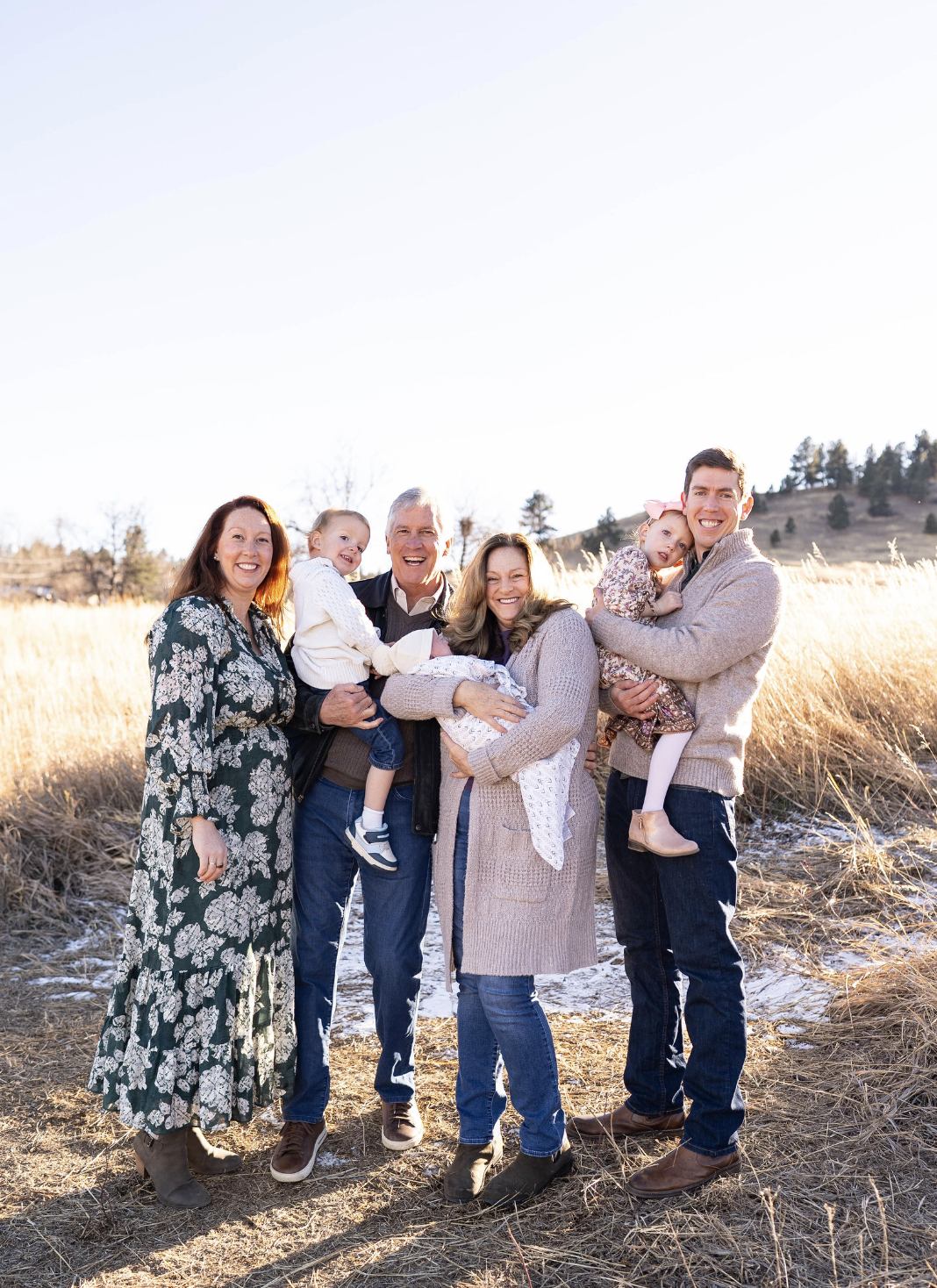Family of six standing outdoors in a field with mountains in the background, smiling at the camera.