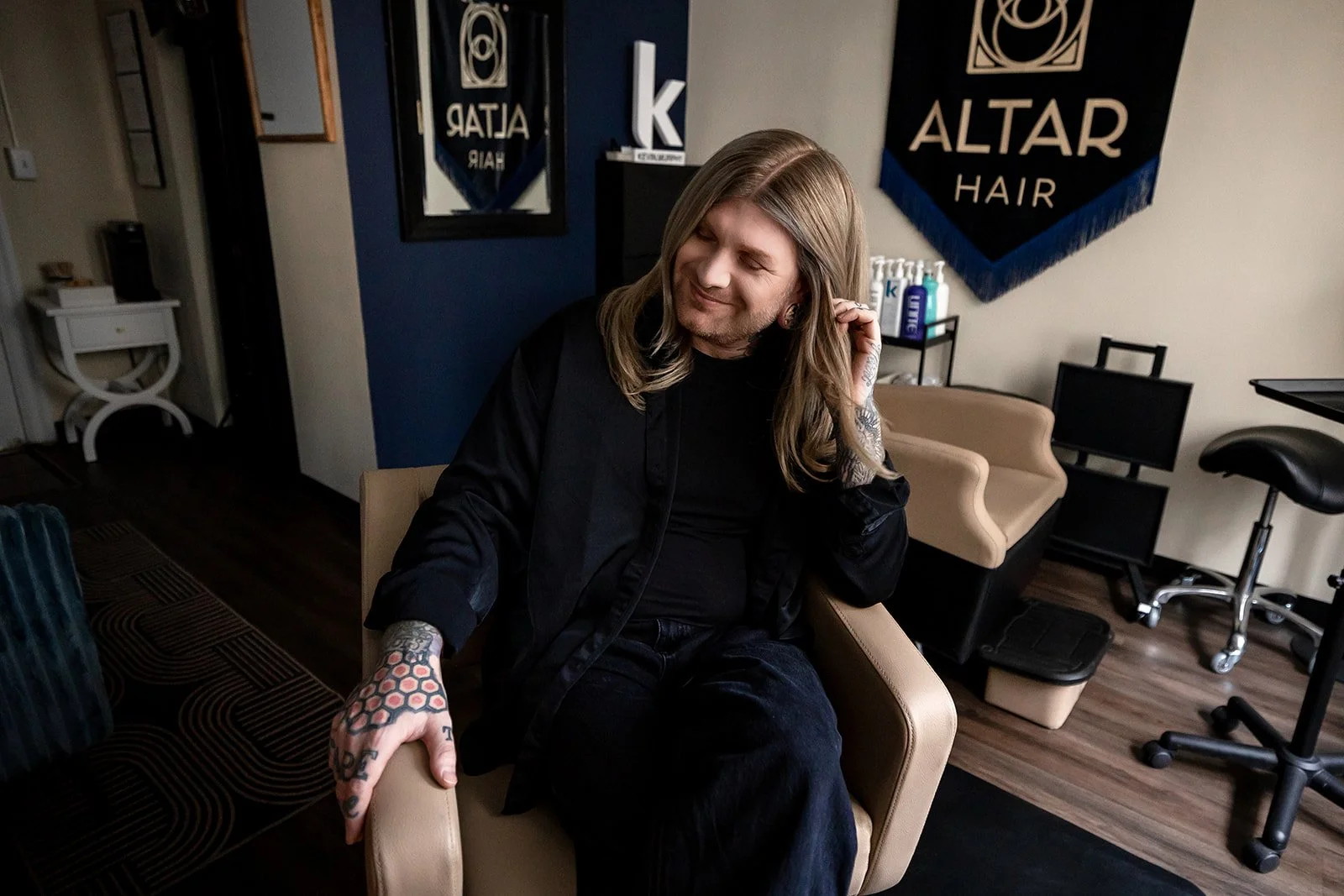 A salon owner sitting in his chair, his business banner hanging behind him