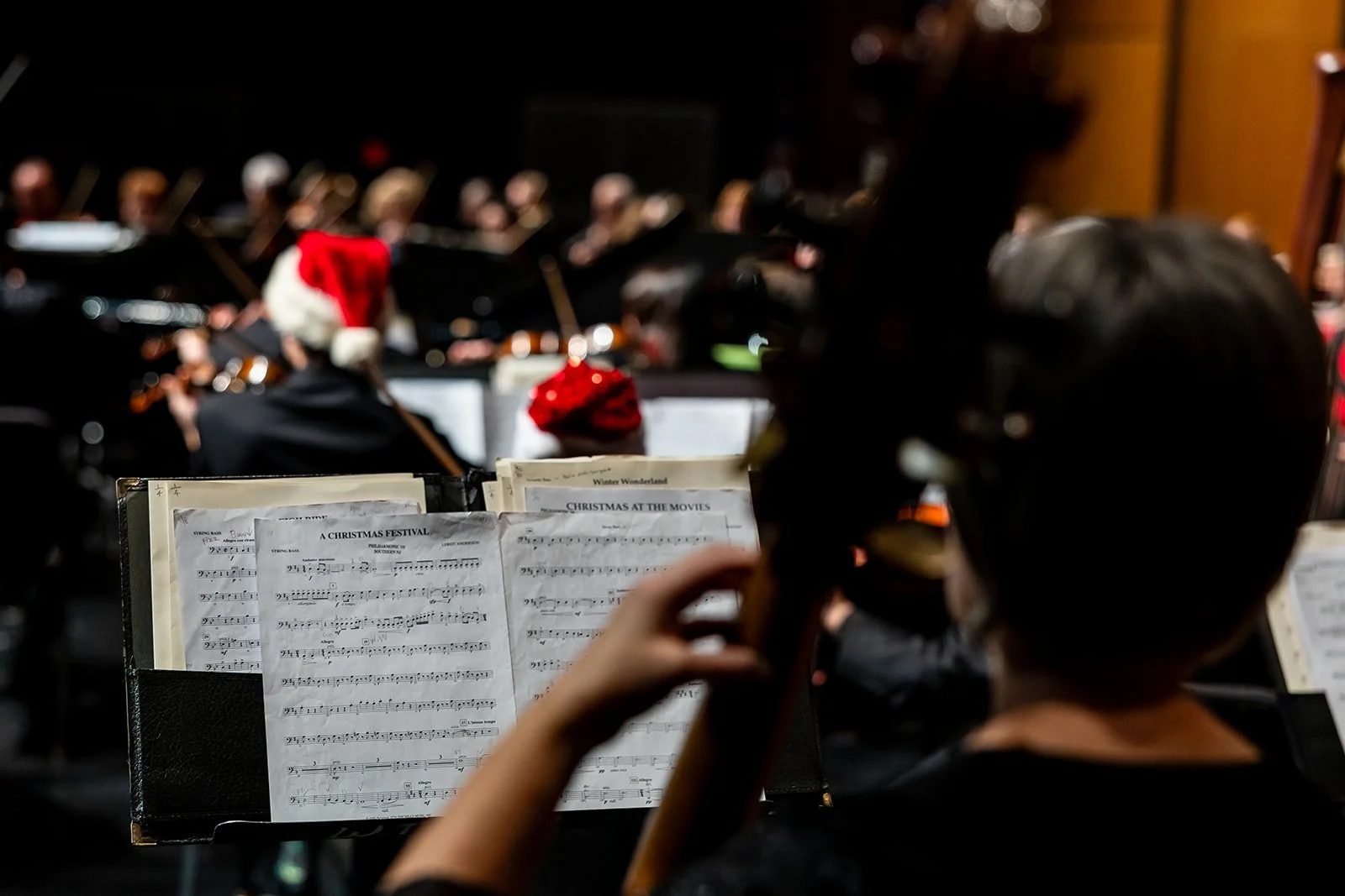 A view of sheet music from behind a bass player, with out of focus view of the rest of the orchestra during a concert