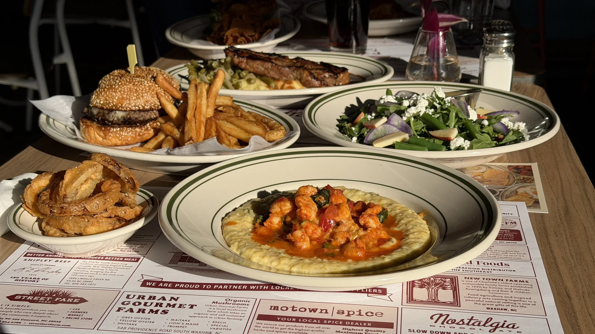 Table spread of Grey's Burger, grilled pork chop, arugula salad, onion rings, and shrimp and grits at Grey's Diner