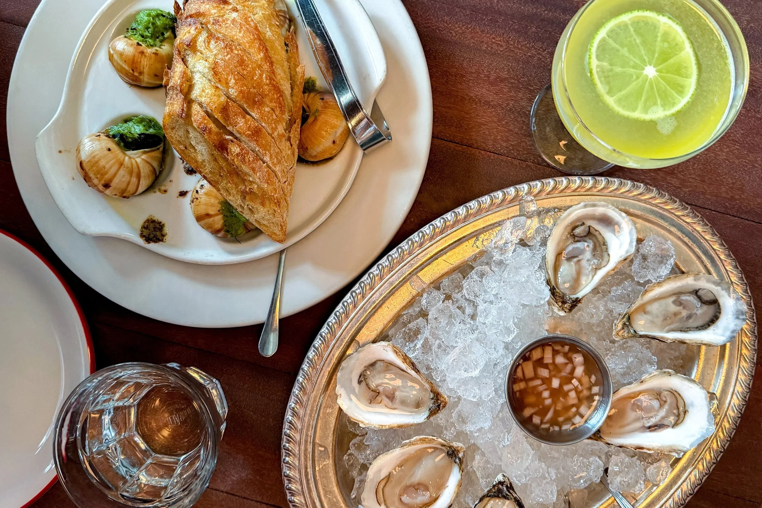 An overhead view of oysters on ice and escargot at The Bull and Beggar in Asheville, with a Dandelion Gimlet cocktail alongside.