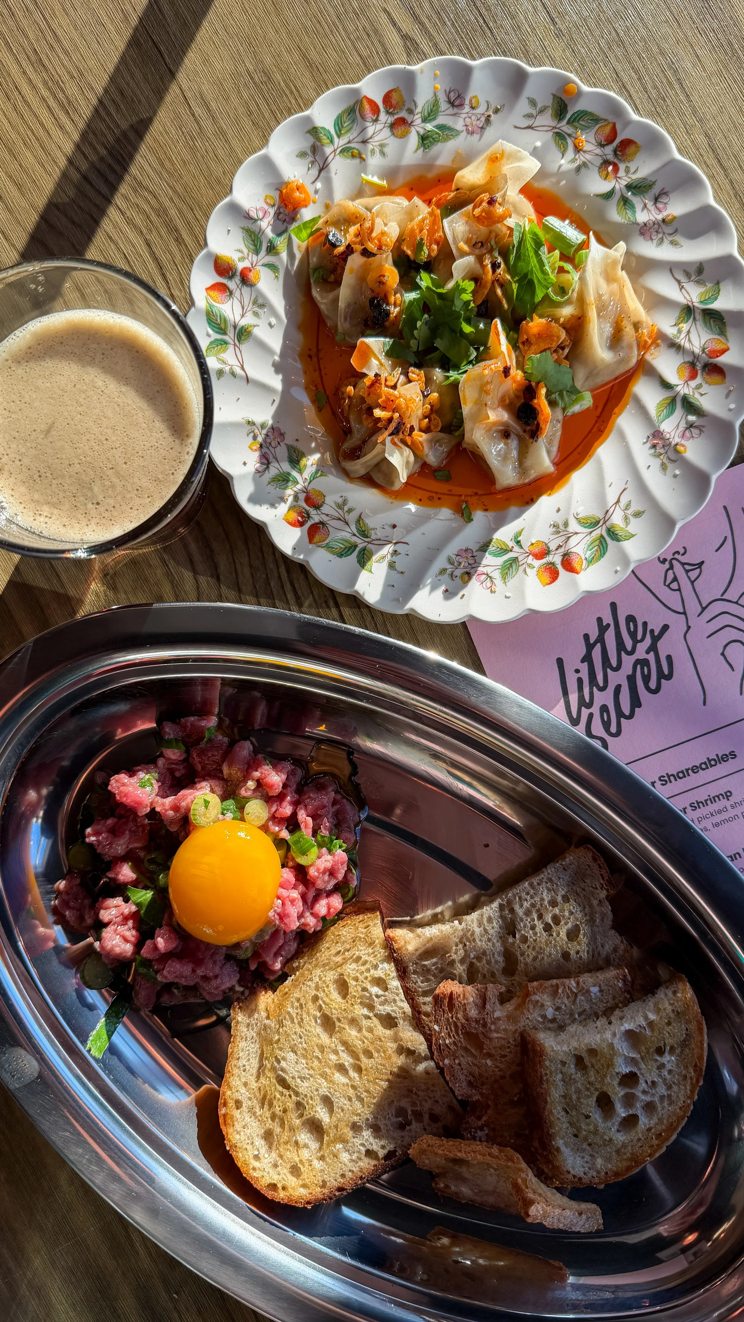 Overhead shot of dumplings in chili oil and beef tartare with egg yolk at Little Secret