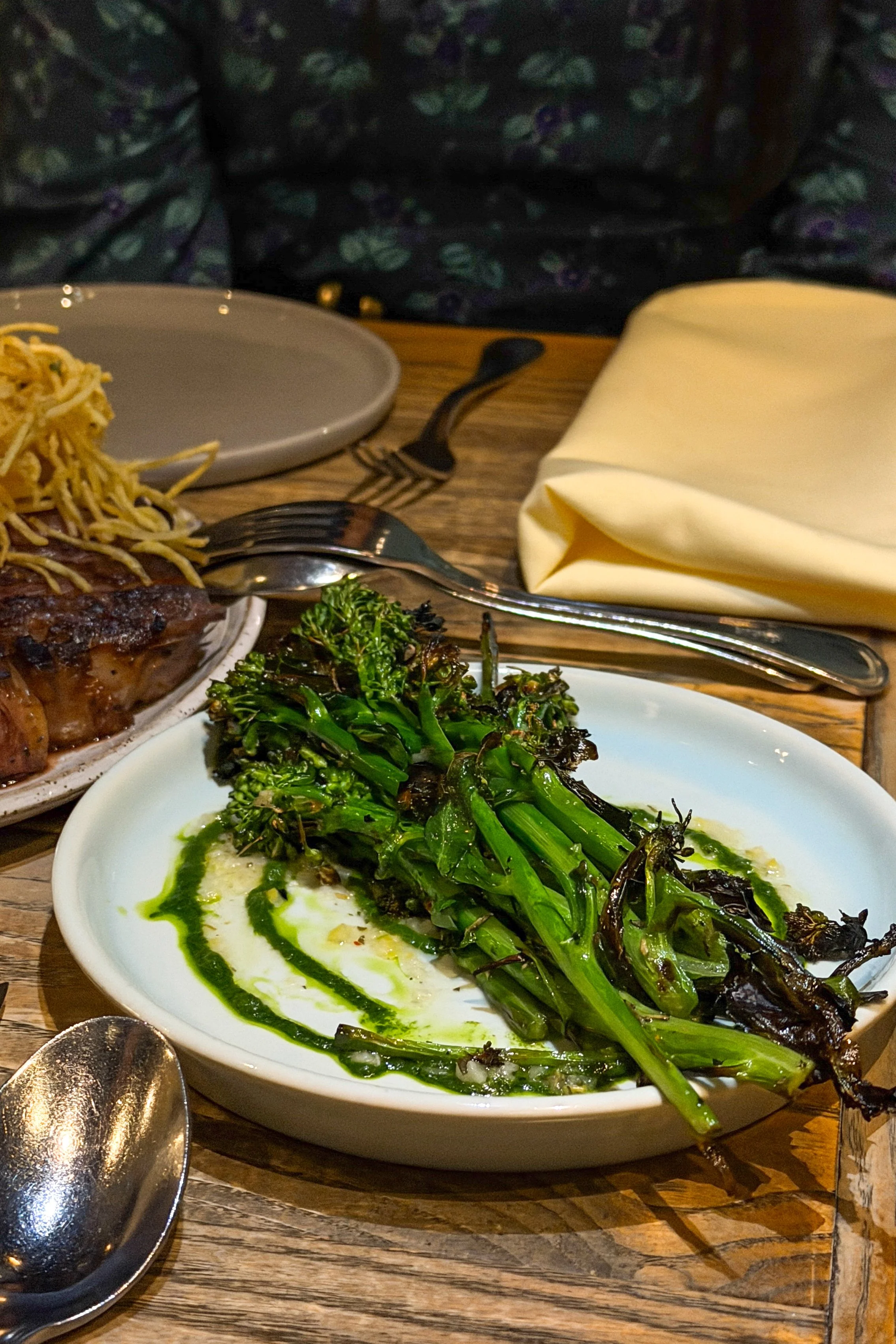 The Grilled Broccolini at J.C. Holdway in Knoxville, charred and drizzled with green sauce, with the wood-fired ribeye in the background