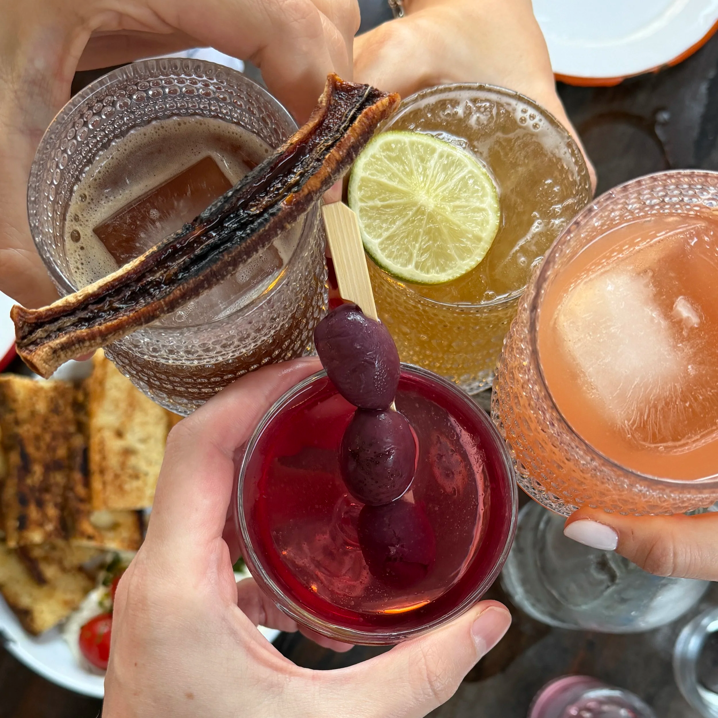 Four cocktails held up in a toast on the patio at Lost Isle