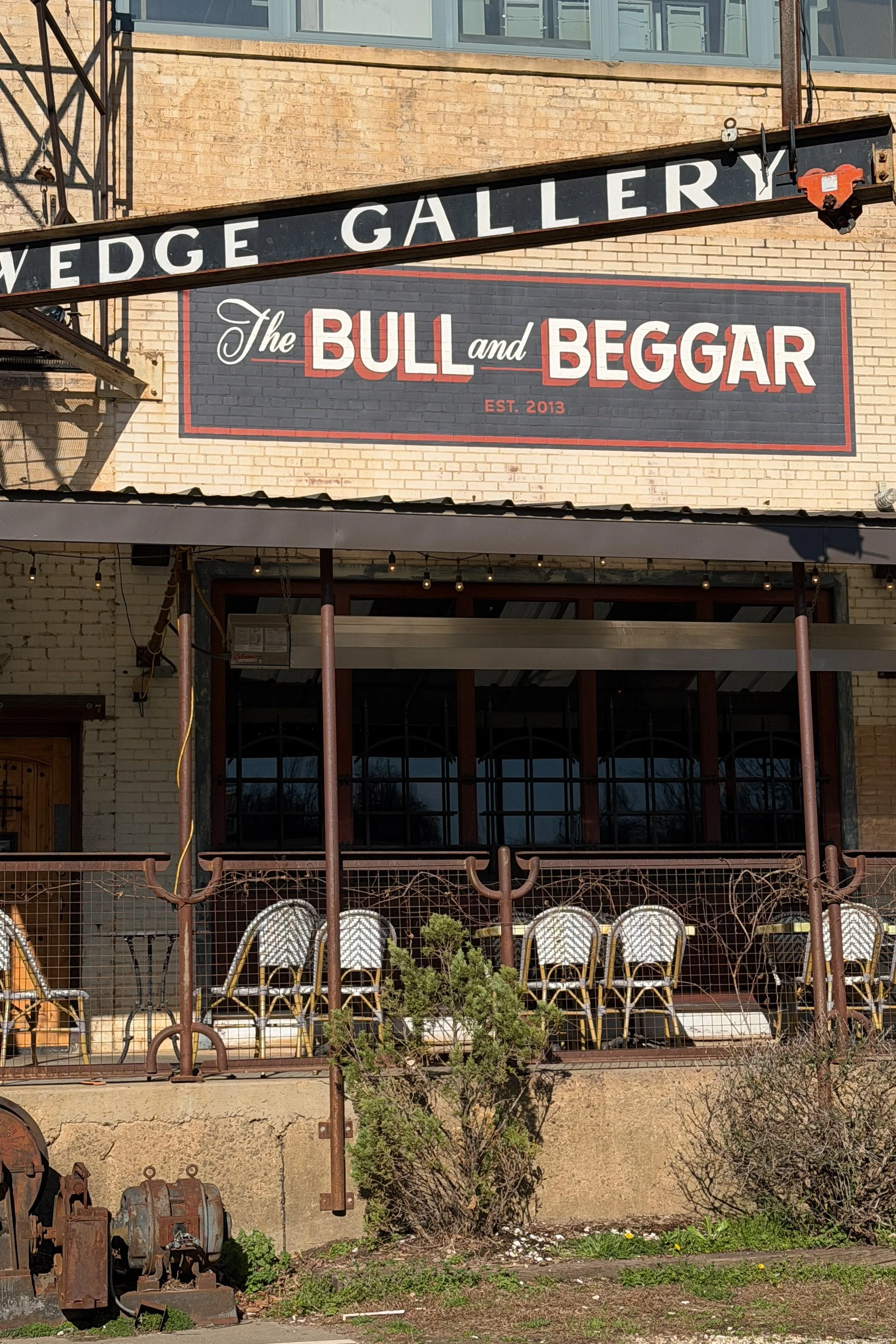 The exterior of The Bull and Beggar in Asheville, with its sign mounted on brick beneath the old Wedge Gallery signage