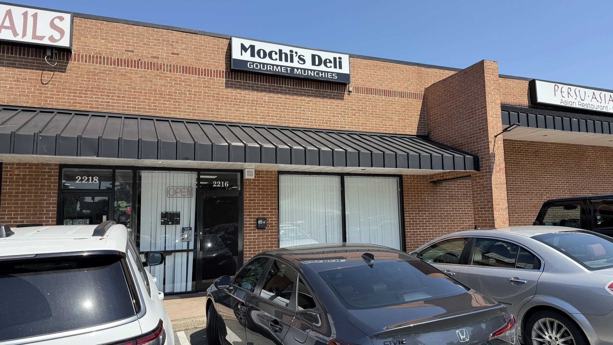 The exterior of Mochi's Deli in Charlotte, tucked into the Dilworth Crossing Shopping Center with blacked-out windows