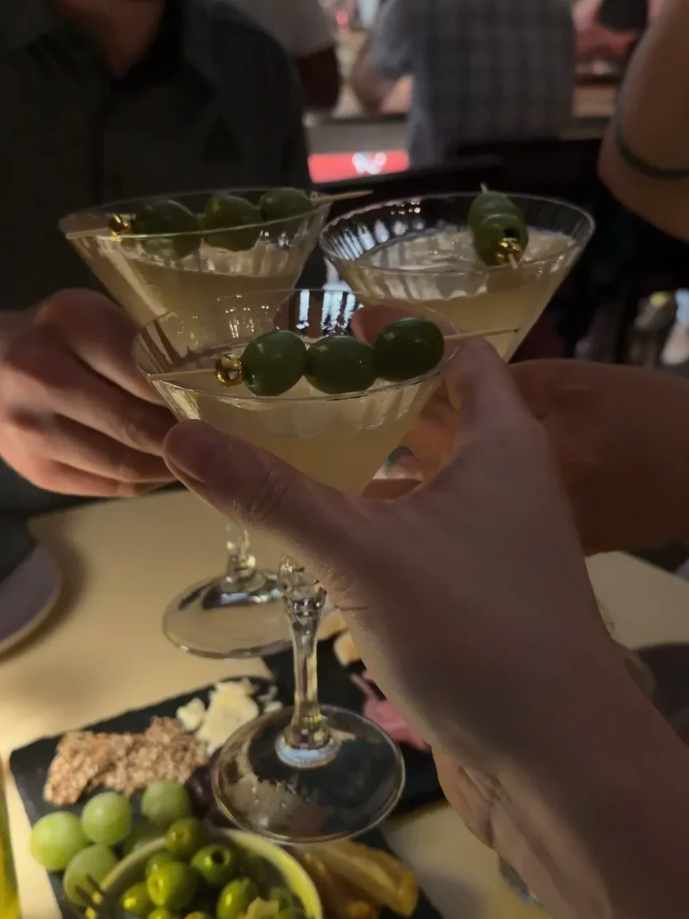 Three Dirty Martinis with olive garnishes toasted together at Lula Drake Wine Parlour
