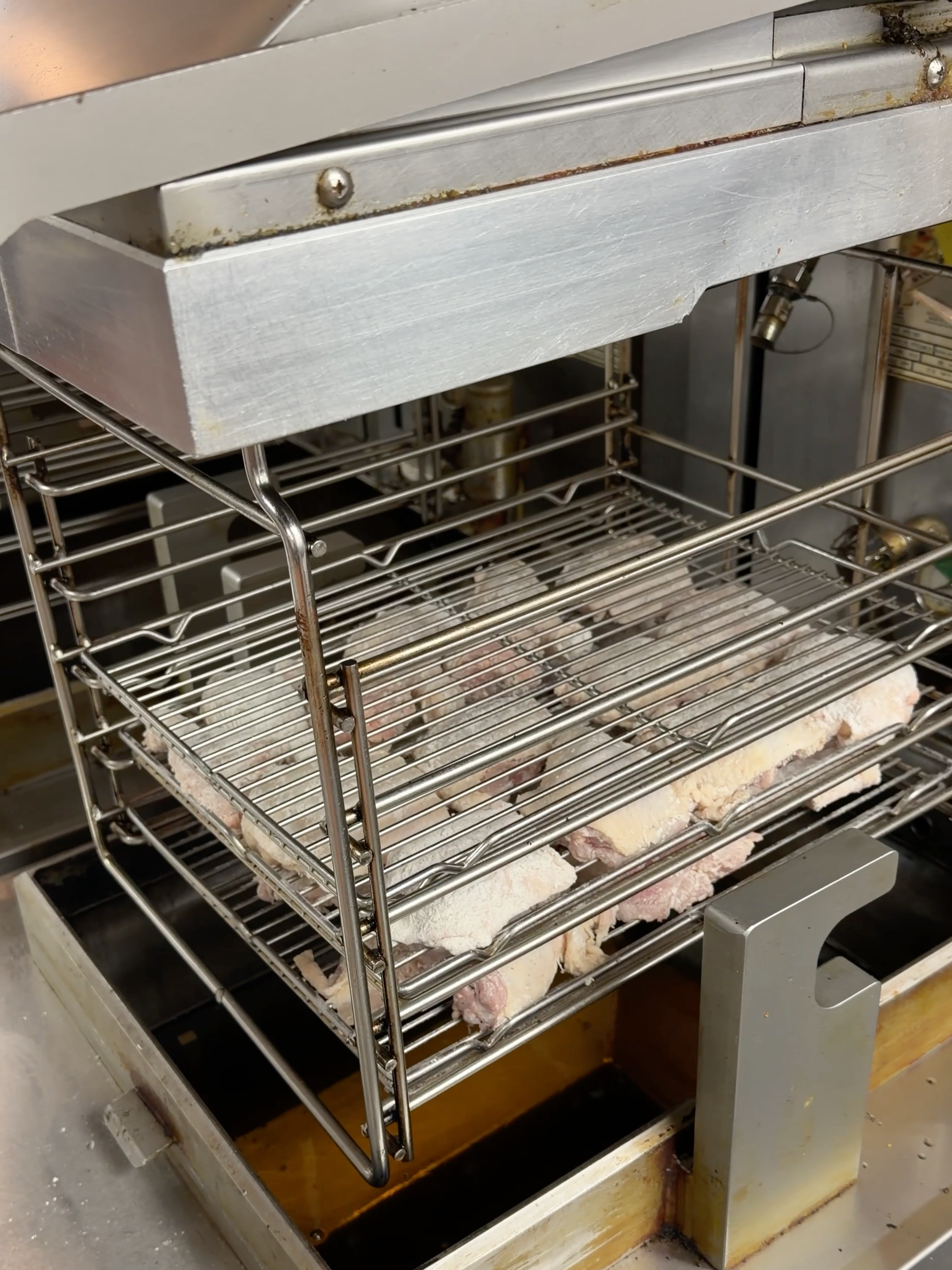 Breaded chicken pieces on a rack before broasting at Bernie's Chicken