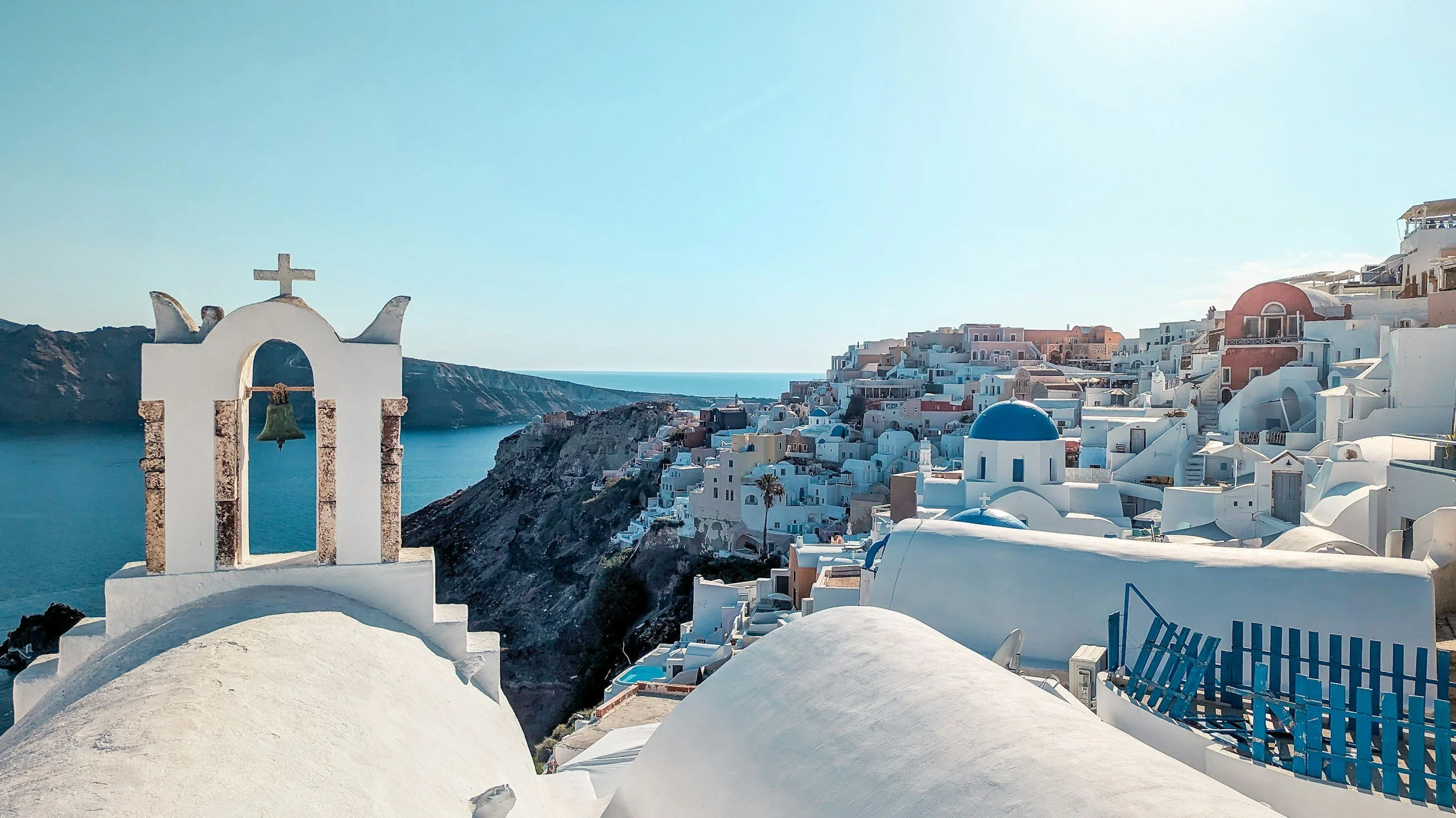 View of Santorini with white buildings, blue-domed churches, and the Aegean Sea in the background.