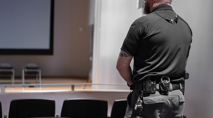A WEKA security guard standing in an empty auditorium, facing away, with a walkie-talkie and keys attached to his belt.