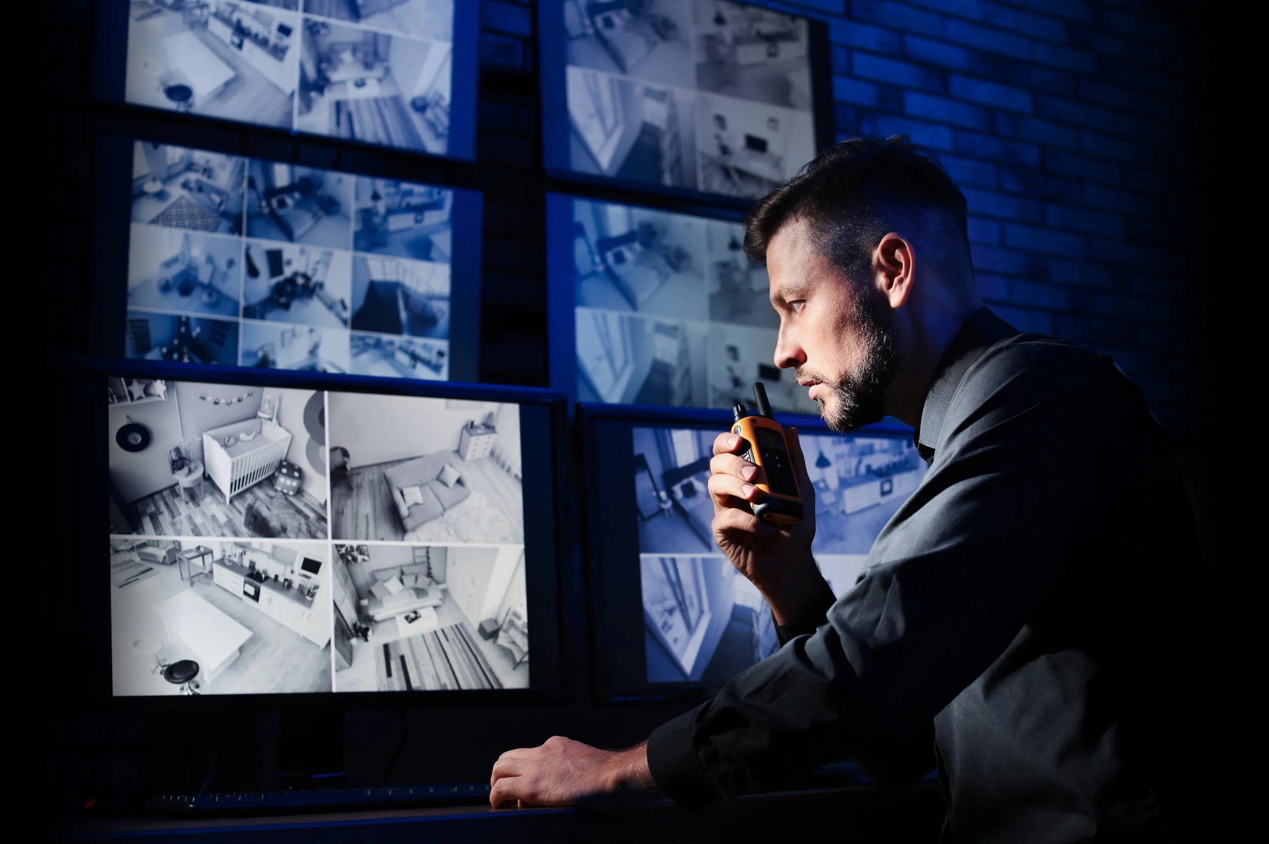 Man looking at multiple surveillance monitor screens displaying different interior spaces.
