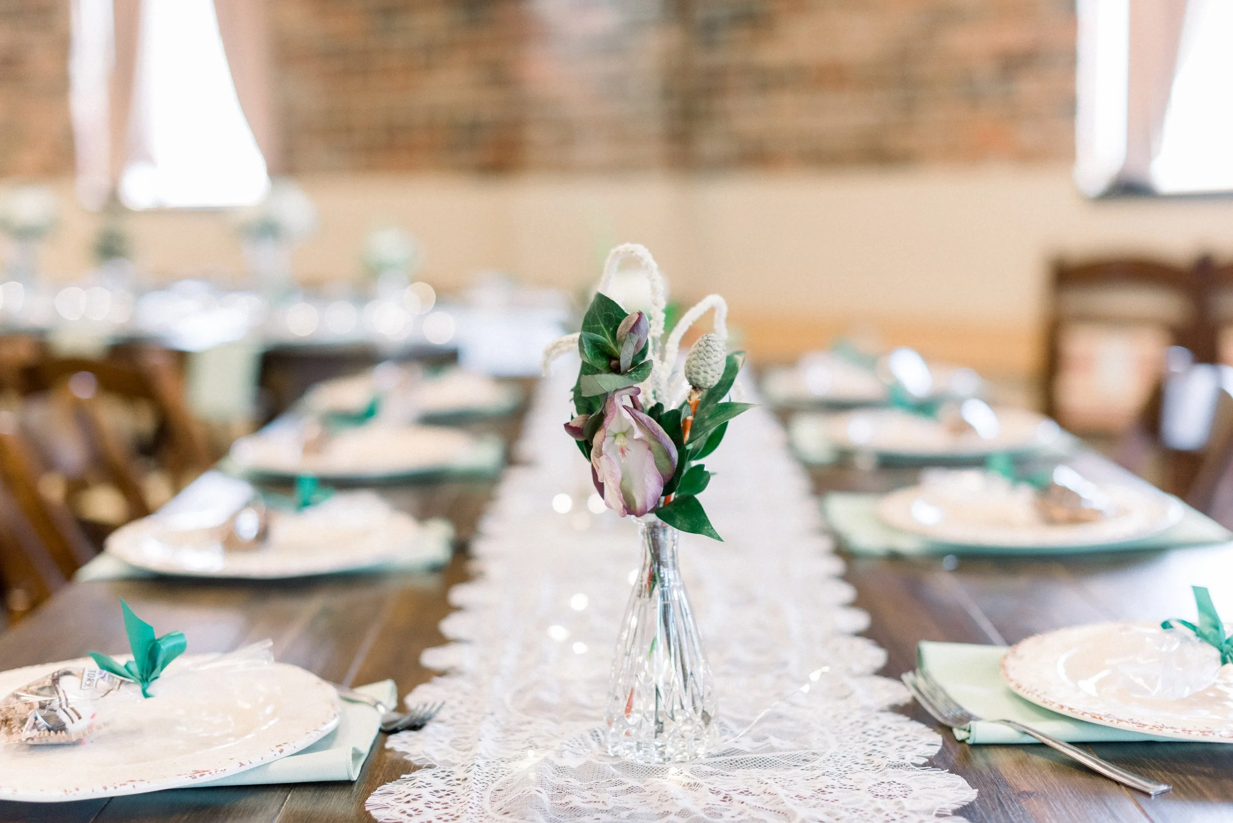 Centerpiece floral arrangement on a table at a decorated event with plates, napkins, and utensils.
