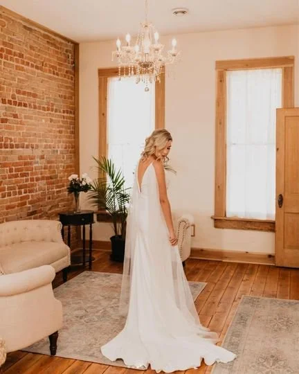 Bride getting ready in Upper Larimer wedding suite with wooden floors, brick and white walls, and a large chandelier.