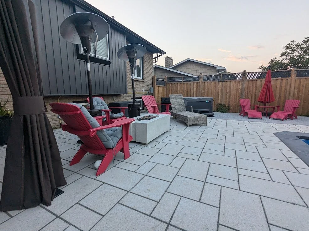 A modern backyard patio featuring Techo-Bloc Blu 60. This St. Catharines project includes a concrete fire pit table, and a hot tub in the background, all enclosed by a wooden privacy fence.