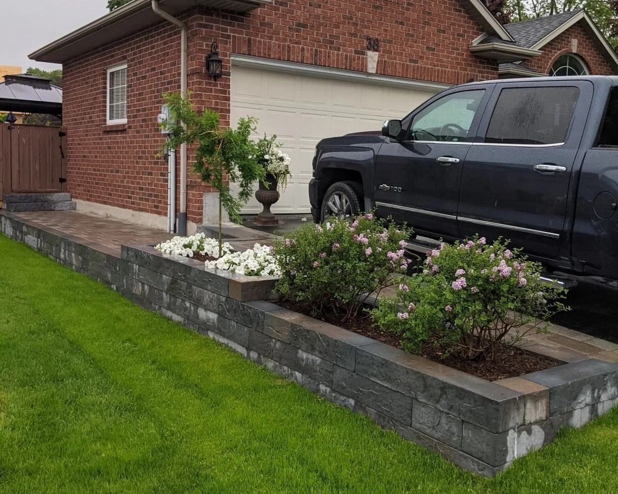 Techo-Bloc Rocka raised stone planter box and retaining wall with Unilock brussels interlock walkway along residential driveway.